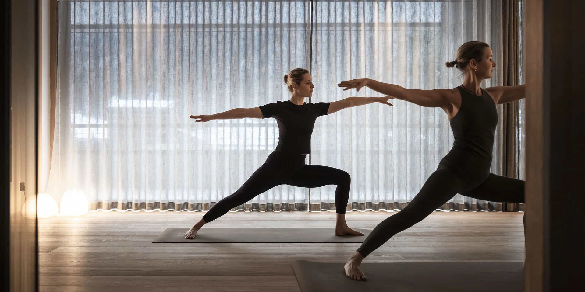 Due donne fanno yoga nella posizione del guerriero in una stanza con tende