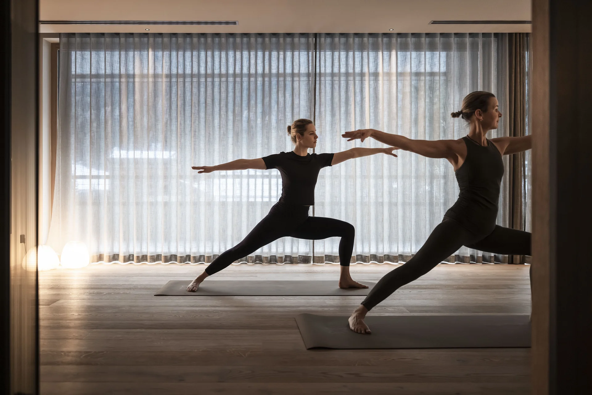 Zwei Frauen machen Yoga in der Kriegerpose in einem Raum mit Vorhängen