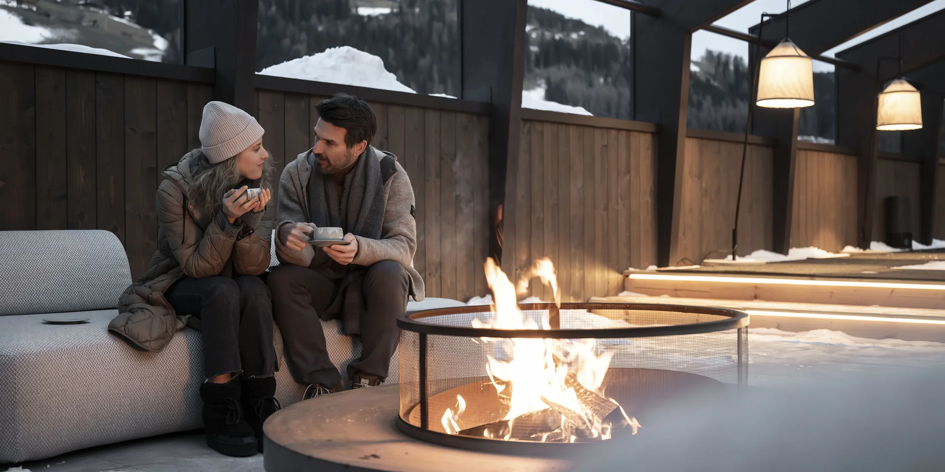Coppia seduta all'aperto vicino al fuoco con bevande calde d'inverno