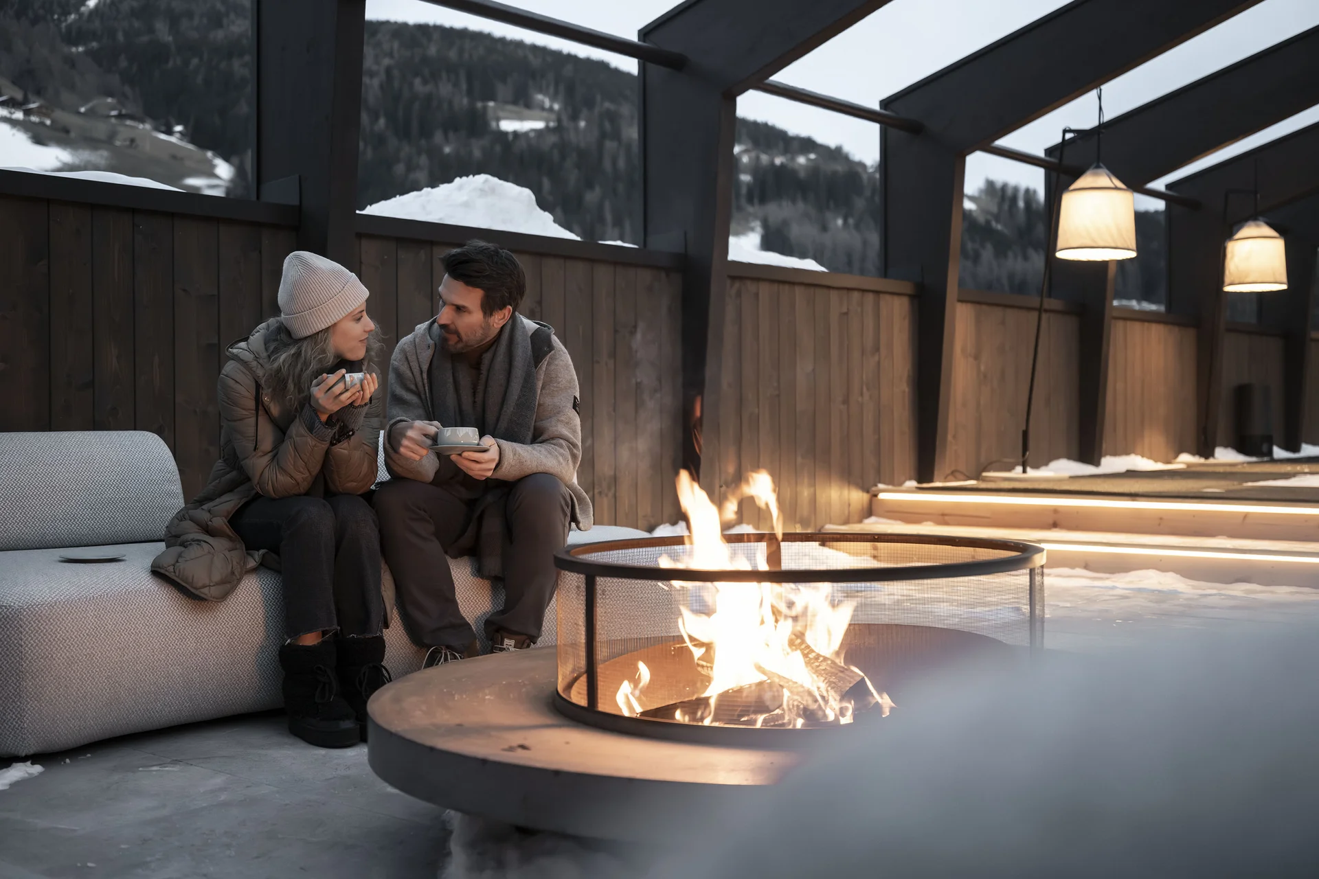 Paar sitzt draußen am Feuer und trinkt heiße Getränke im Winter