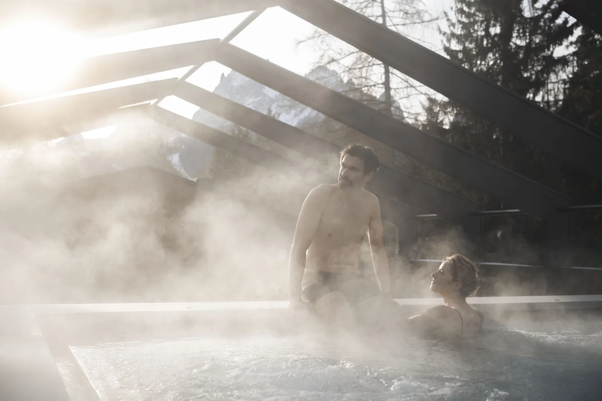 Mann und Frau entspannen in dampfendem Außenwhirlpool bei Sonnenuntergang