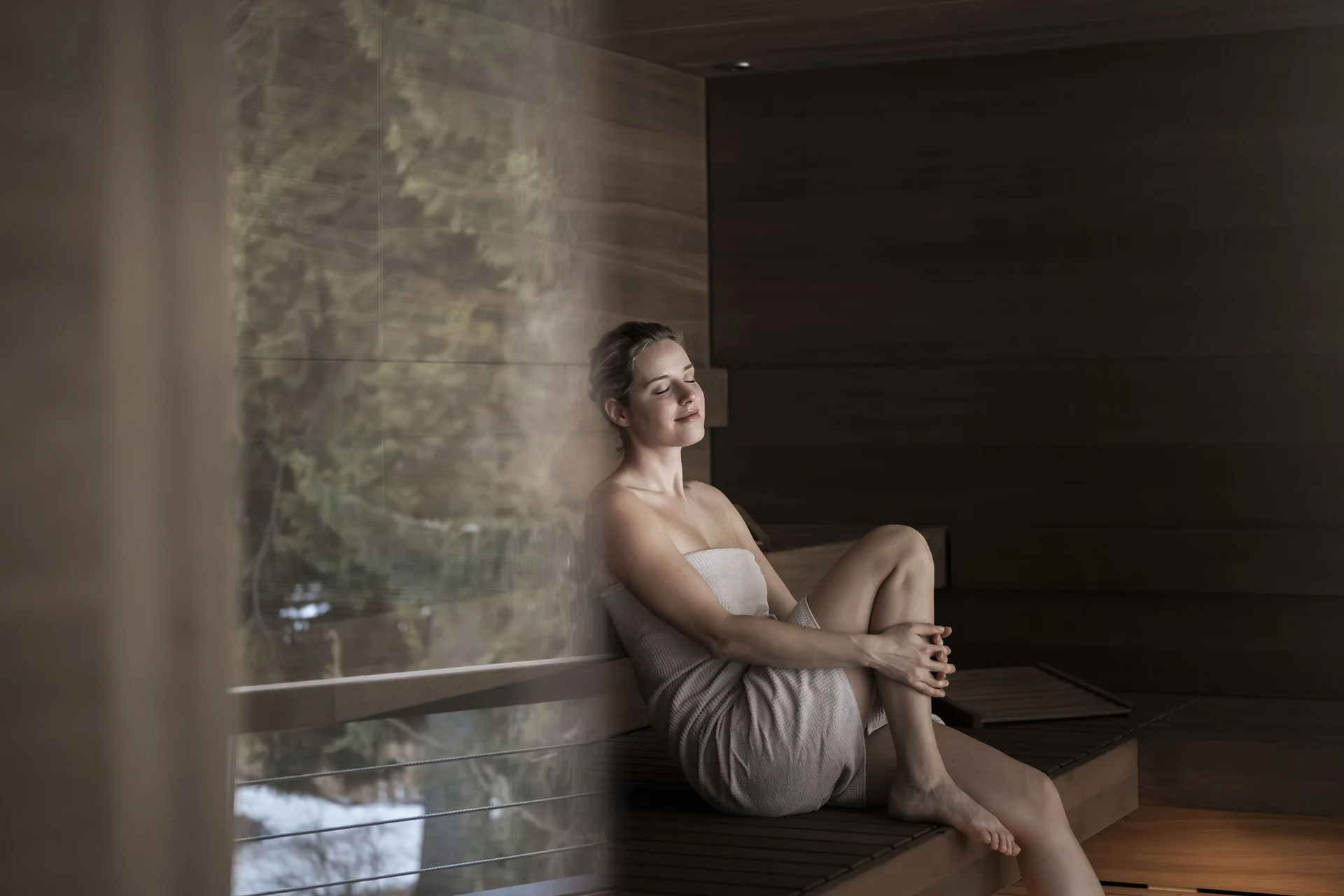 Frau entspannt in Sauna mit Handtuch und geschlossenen Augen