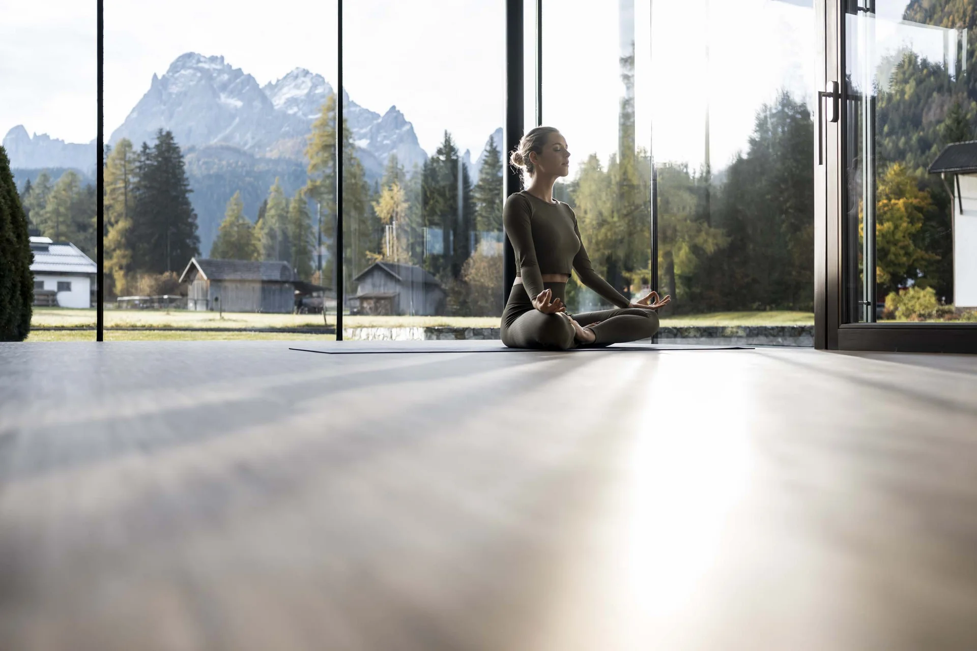 Frau meditiert drinnen vor Panoramafenstern mit Bergblick