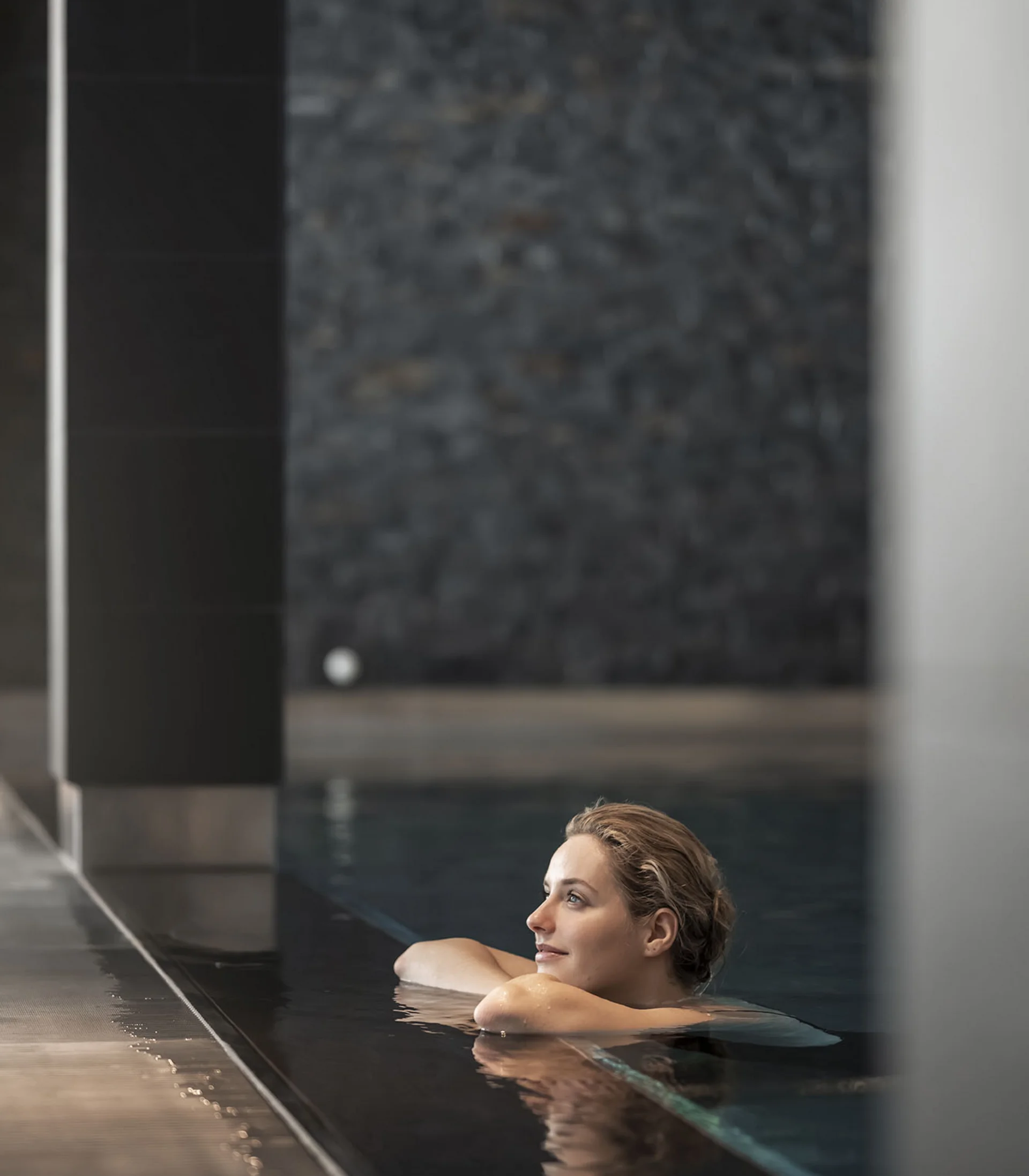 Donna rilassata in piscina interna con parete in pietra sullo sfondo