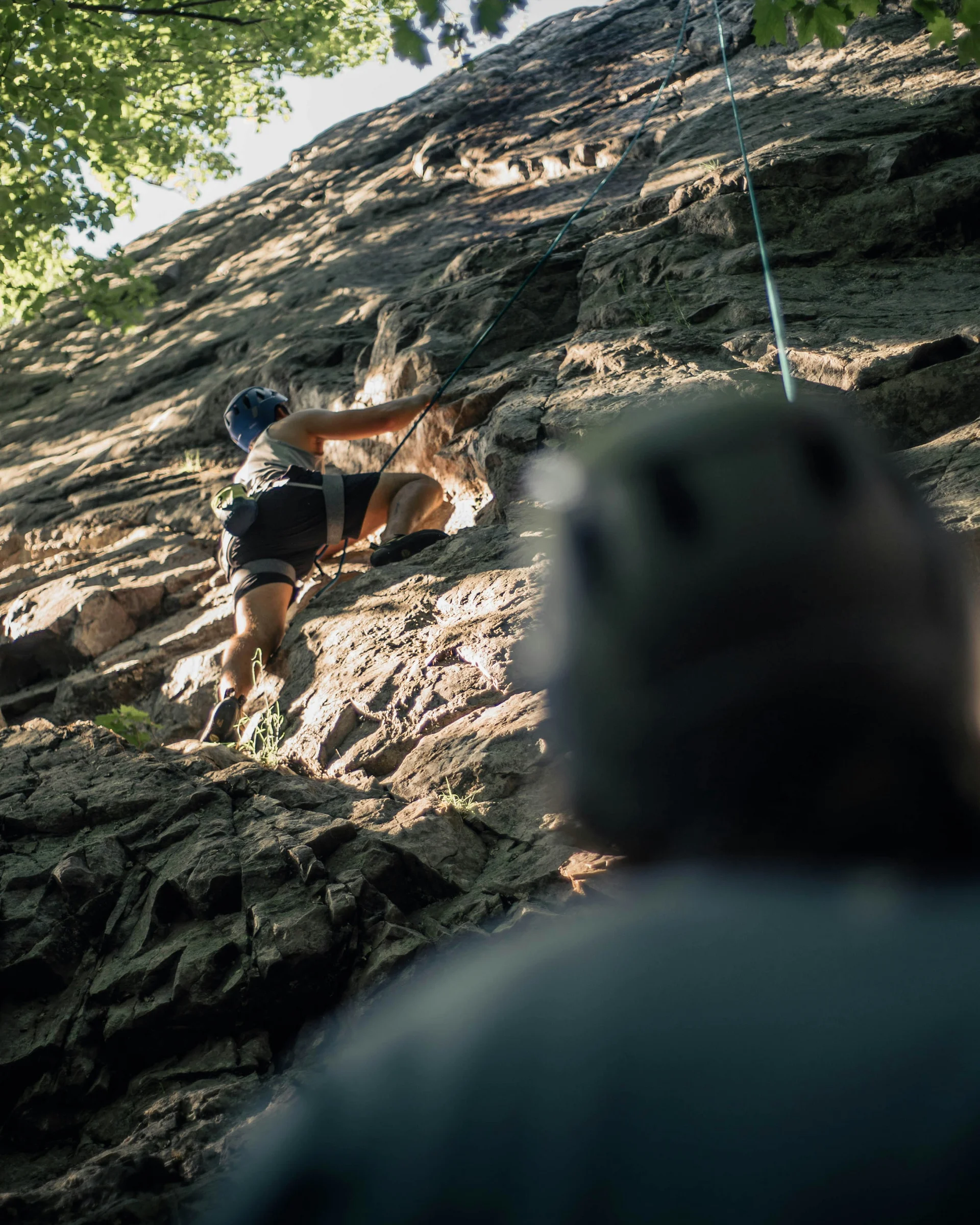 Person klettert an einem Felsen, eine zweite Person sichert von unten