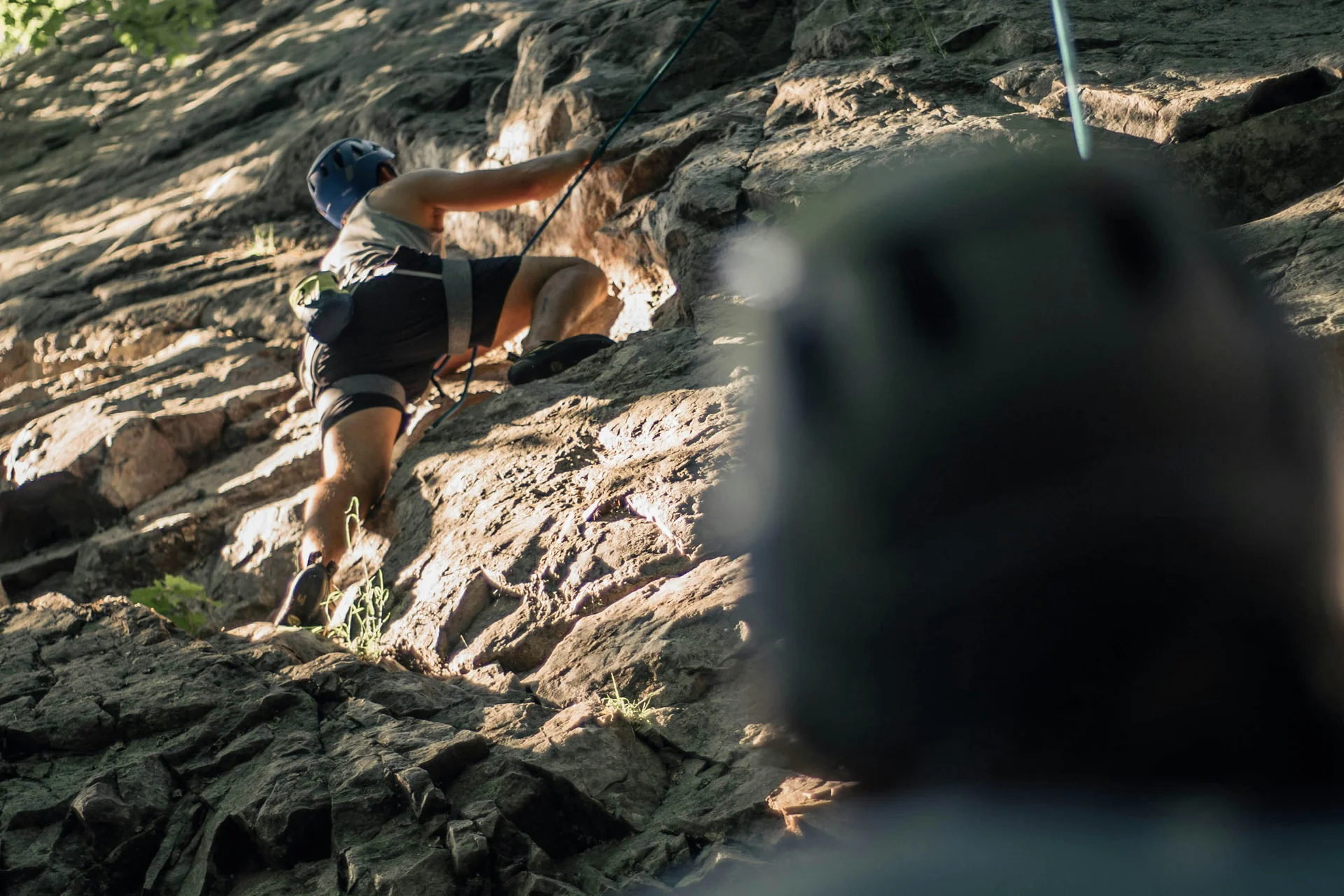 Persona che arrampica una roccia con un'altra che assicura dal basso