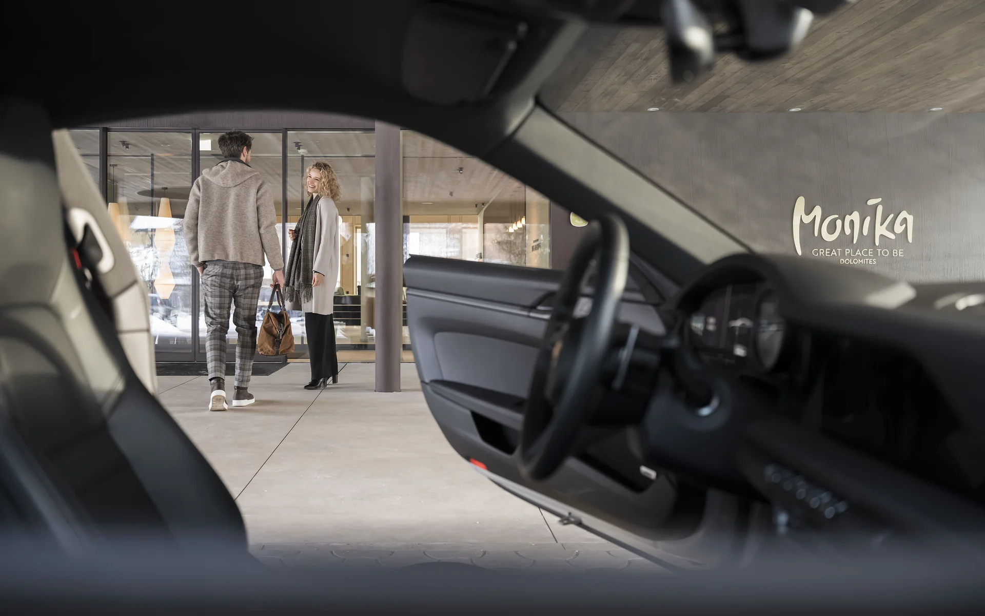 Blick durch ein Auto auf zwei Menschen vor einem Gebäude mit Monika-Logo