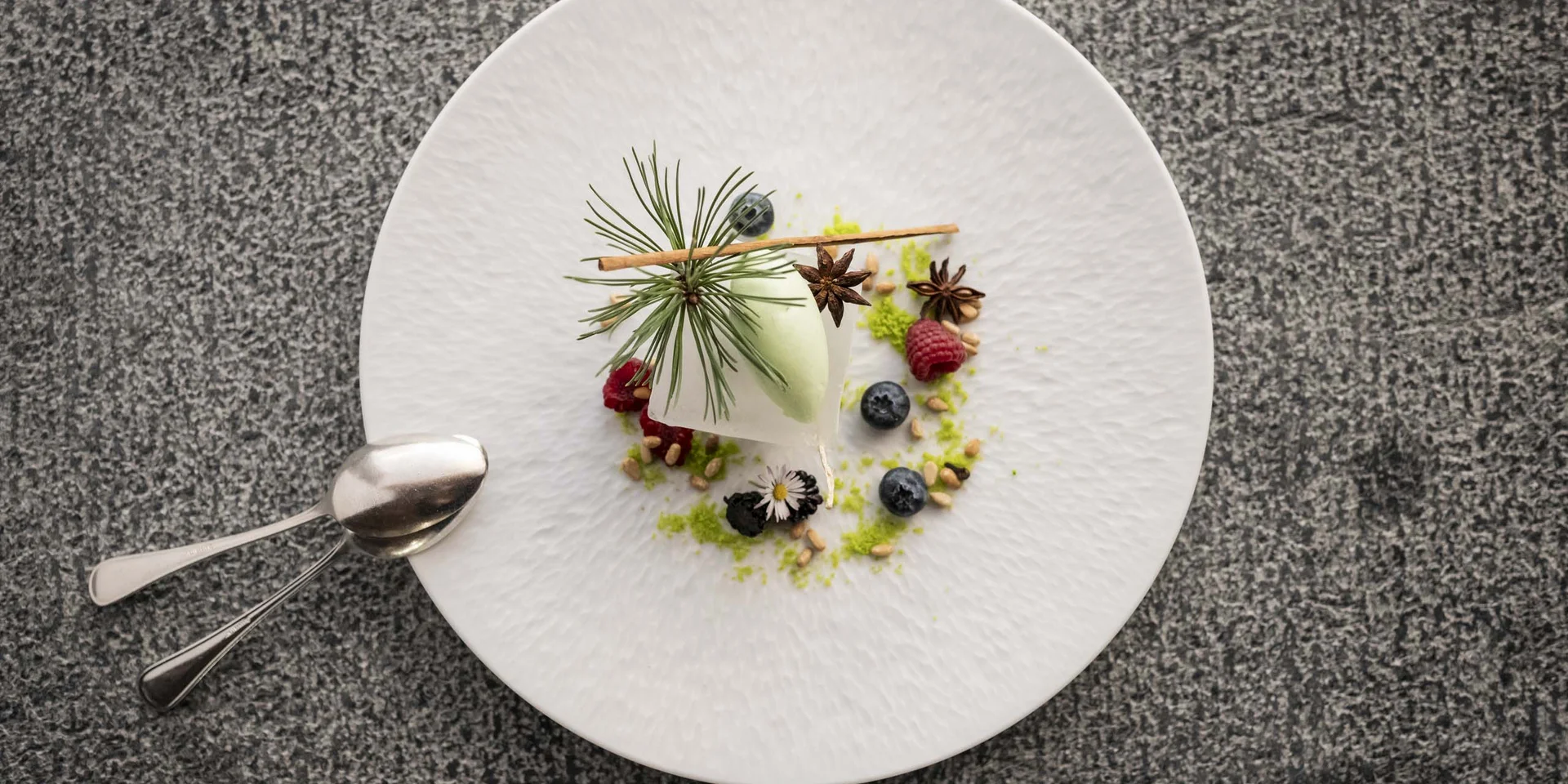 Kunstvoll angerichtetes Dessert mit Beeren, Gewürzen und Kräutern auf weißem Teller