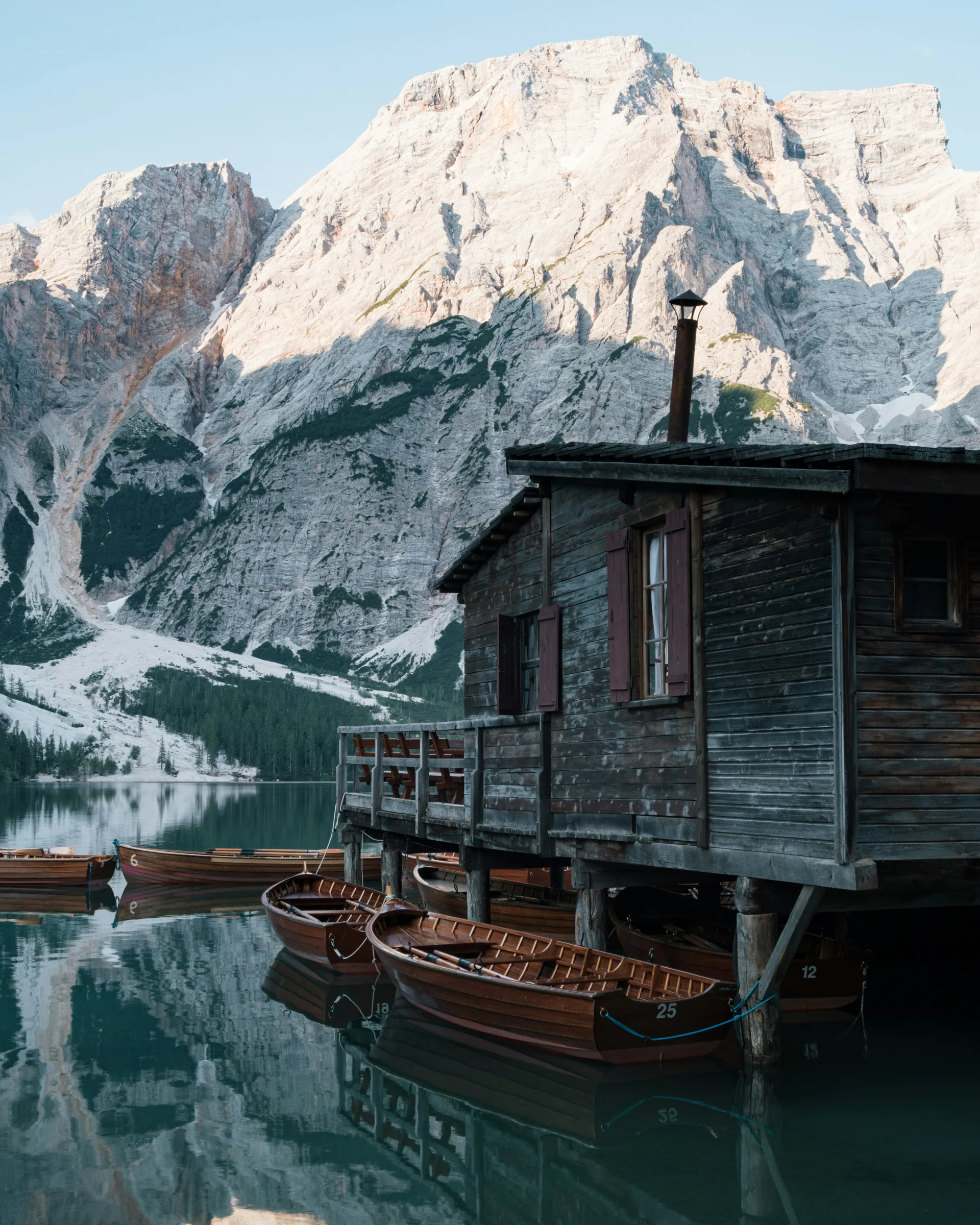 Holzboote liegen an einer Hütte auf einem Bergsee mit Alpengipfeln im Hintergrund
