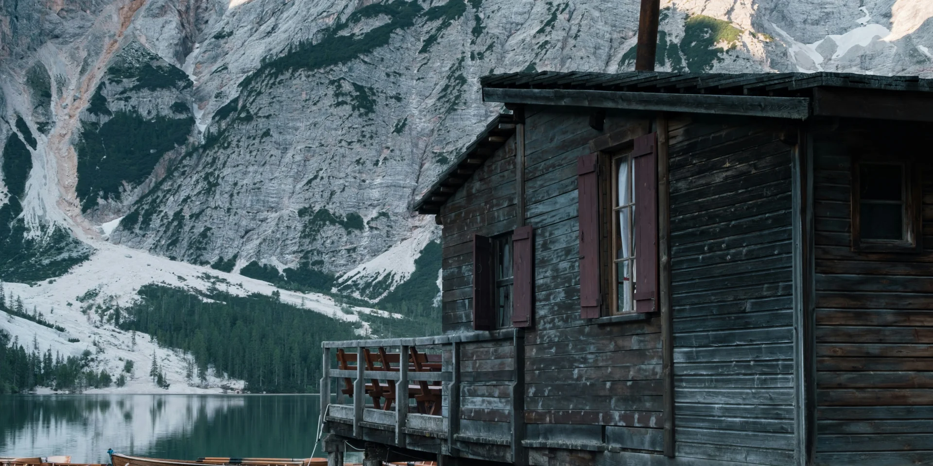 Holzboote liegen an einer Hütte auf einem Bergsee mit Alpengipfeln im Hintergrund
