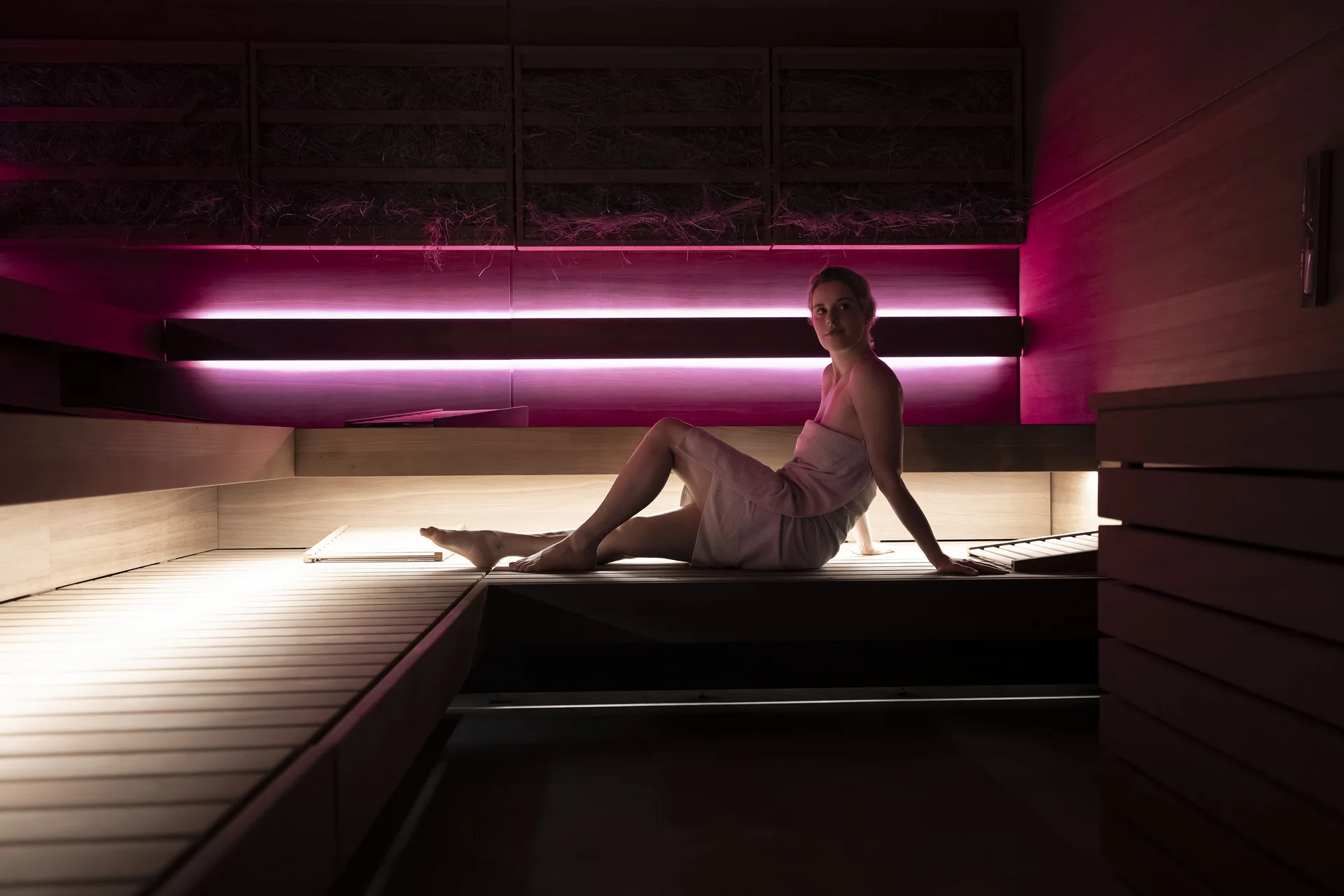 Frau sitzt entspannt in moderner Sauna mit rosa Beleuchtung