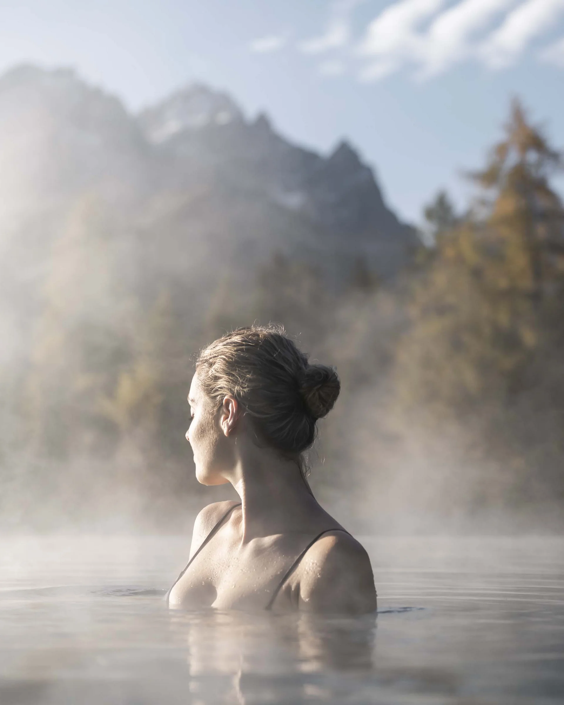 Frau entspannt im heißen Thermalwasser mit nebeligem Bergpanorama im Hintergrund