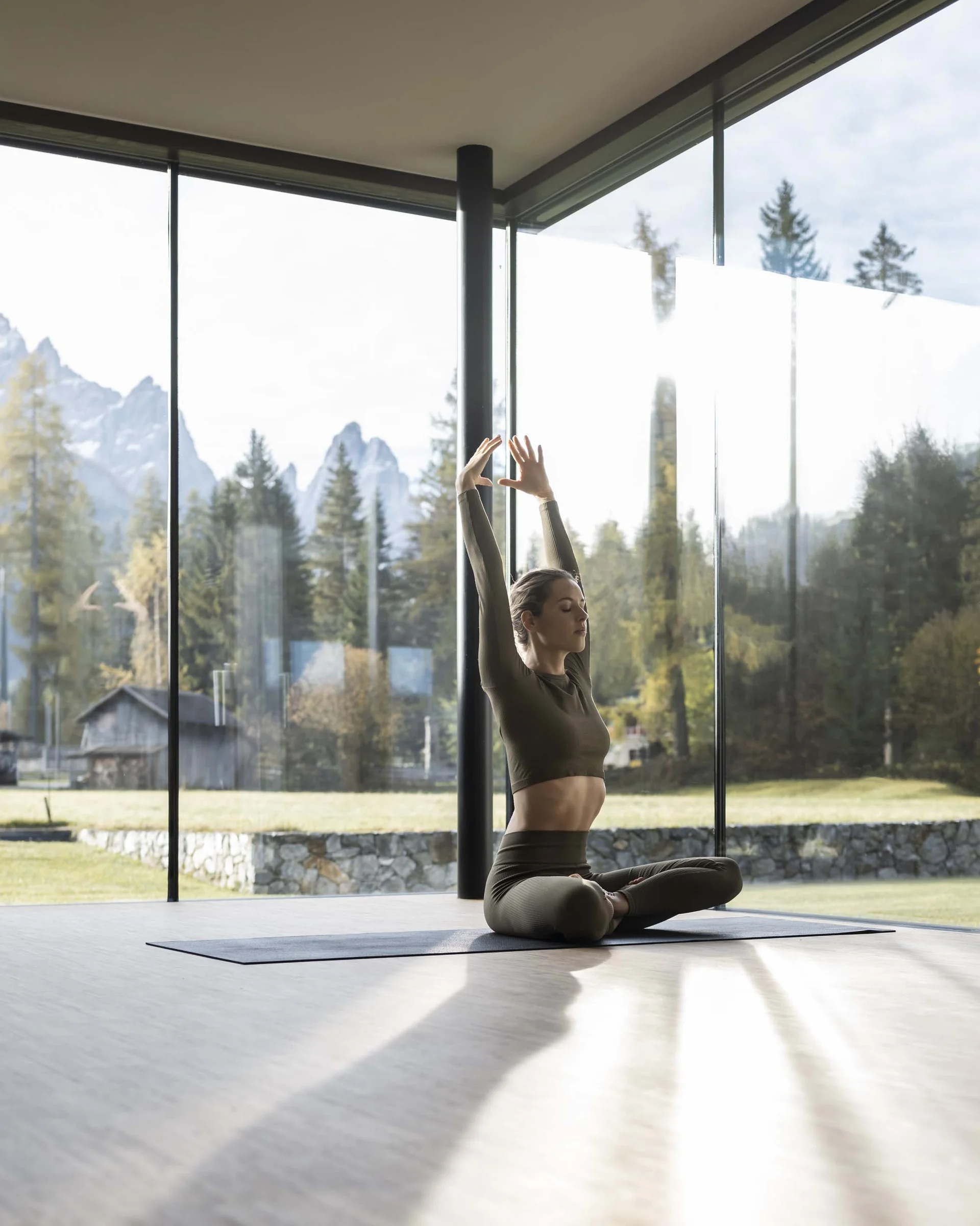Frau macht Yoga im modernen Raum mit Bergblick durch große Fenster
