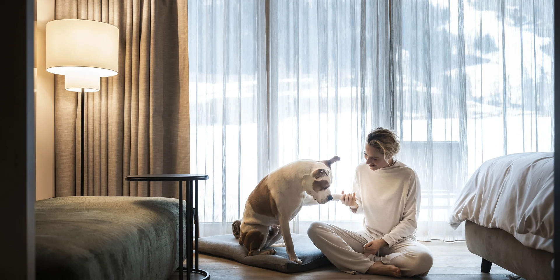 Donna che dà la zampa al cane seduta sul pavimento davanti a una finestra con tende