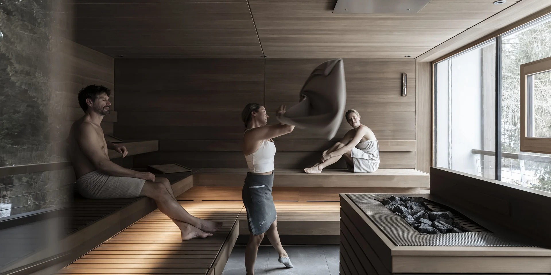Tre persone rilassate in una sauna con grandi finestre.