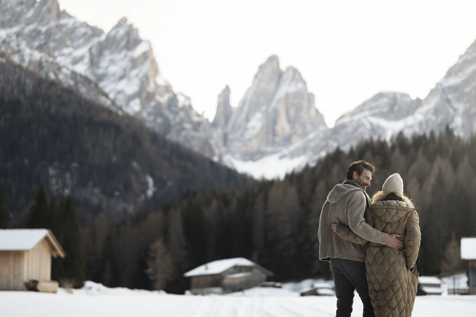 Couple hugging in snowy mountain landscape with wooden cabins