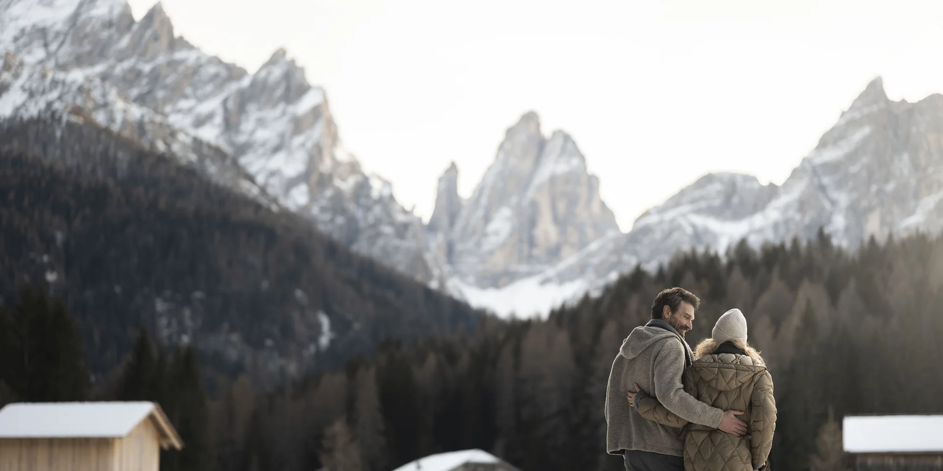 Coppia abbracciata in paesaggio innevato con montagne e baite