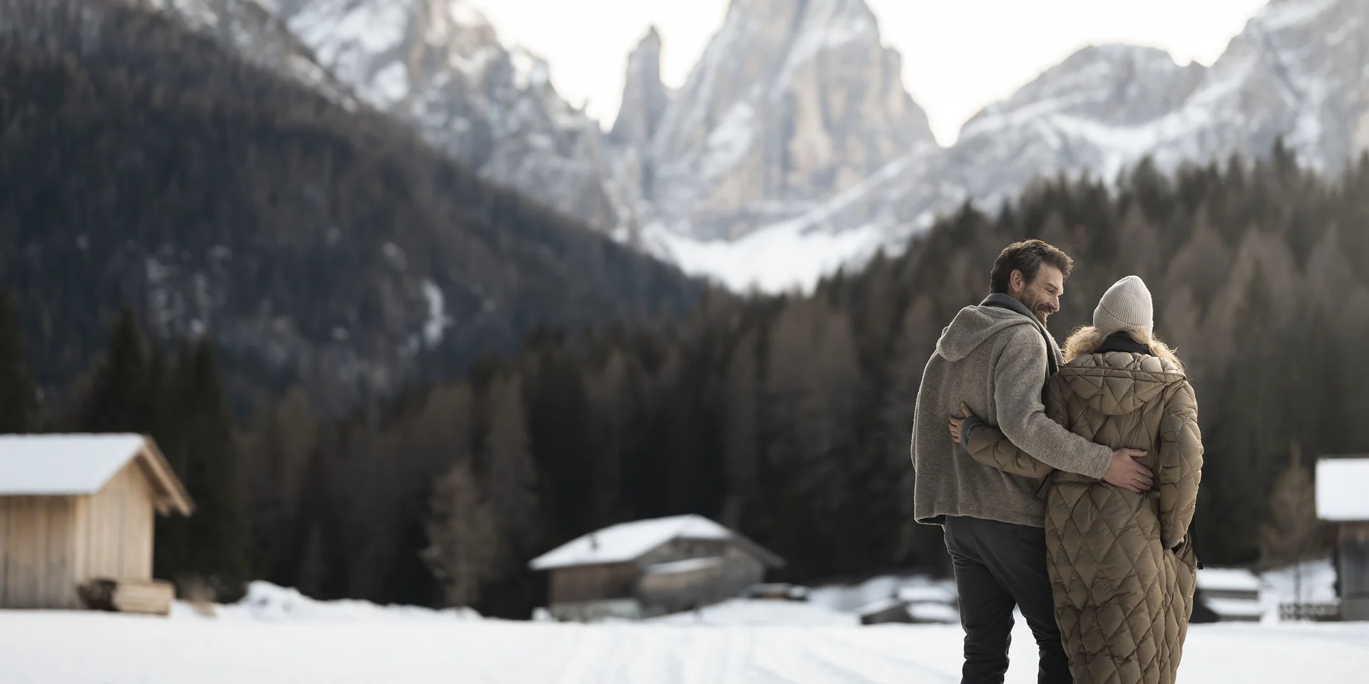 Couple hugging in snowy mountain landscape with wooden cabins