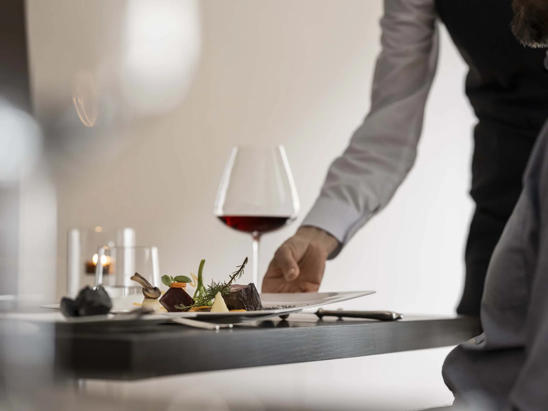 Hotel Monika: das romantische Hotel in Südtirol Kellner serviert gehobenes Gericht mit Rotwein an Restauranttisch