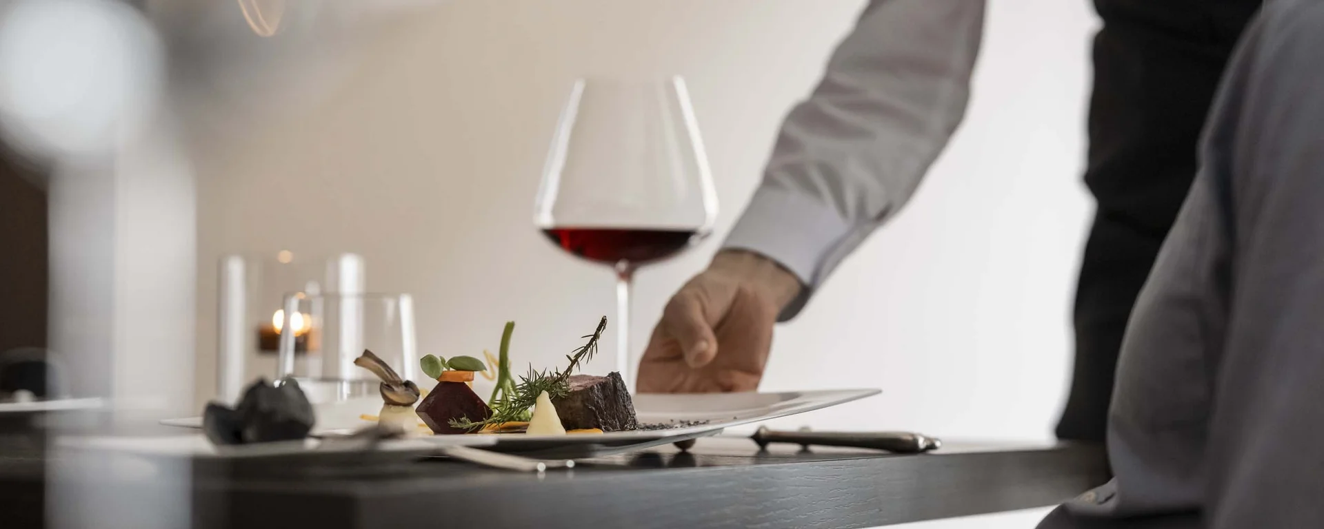 Offene Stellen im Hotel Monika Kellner serviert gehobenes Gericht mit Rotwein an Restauranttisch