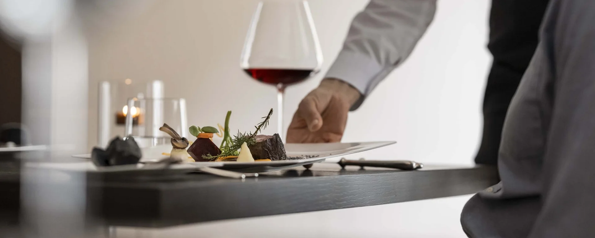 À-la-carte-Restaurant CANA in Sexten Kellner serviert gehobenes Gericht mit Rotwein an Restauranttisch