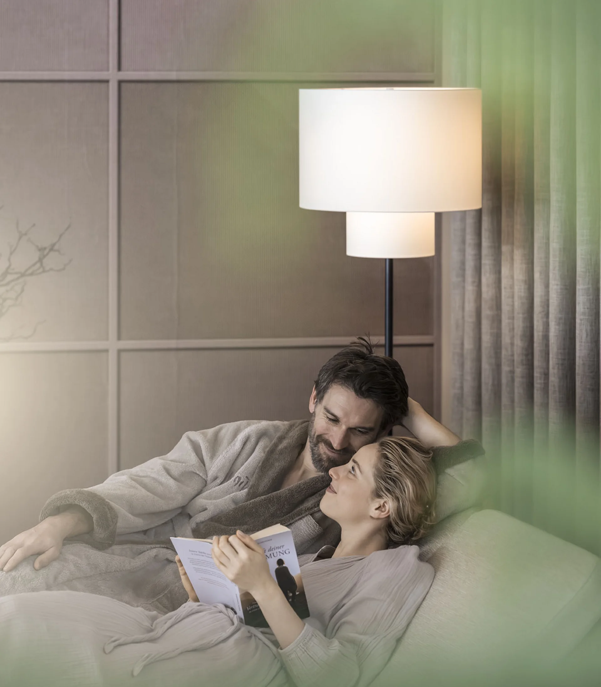 Coppia rilassata sul divano, donna legge un libro, uomo la guarda con amore