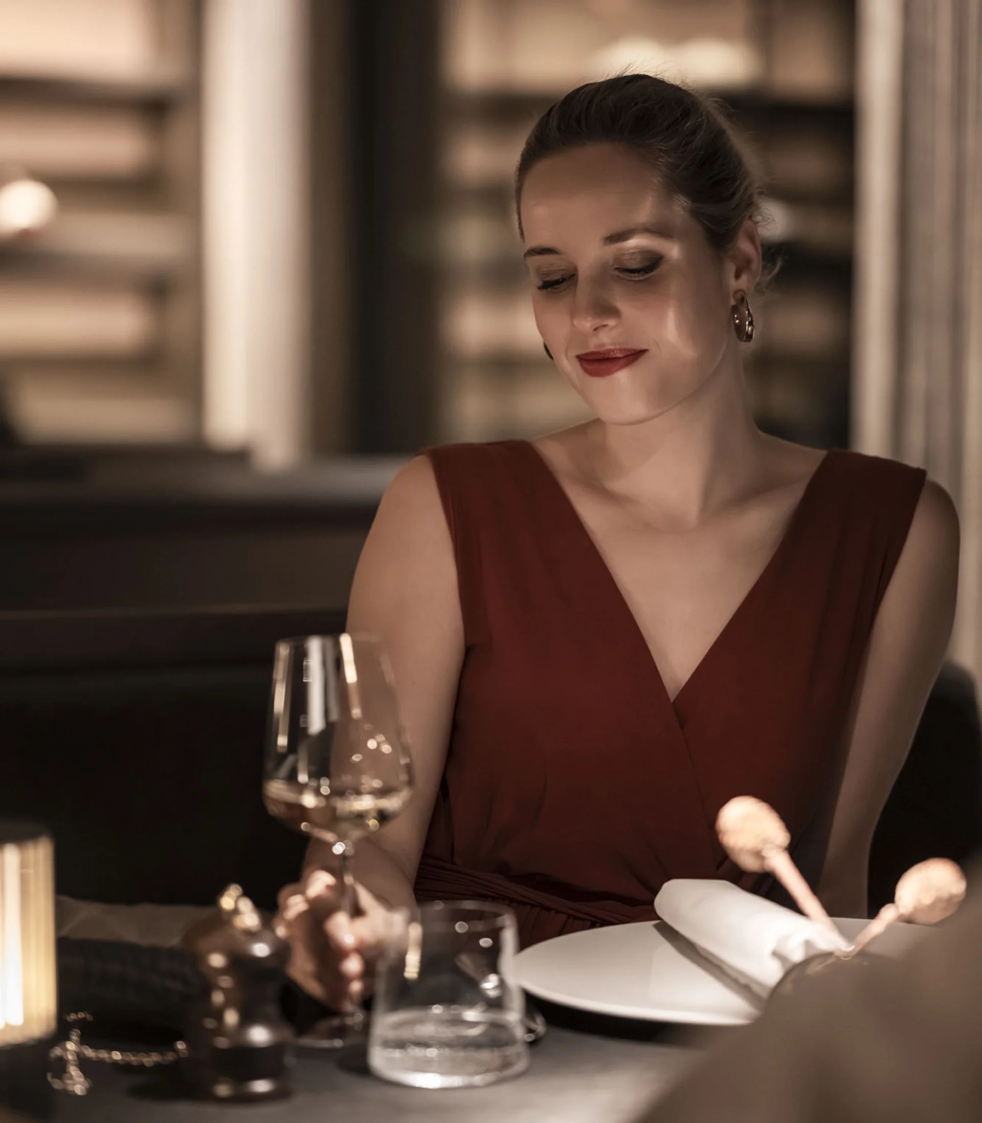 Donna in abito rosso con calice di vino in ristorante elegante