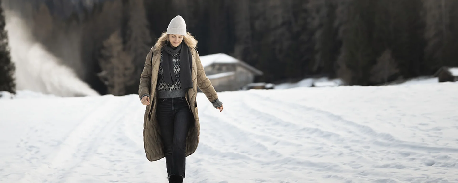 Donna con abbigliamento invernale che cammina su campo innevato con montagne sullo sfondo