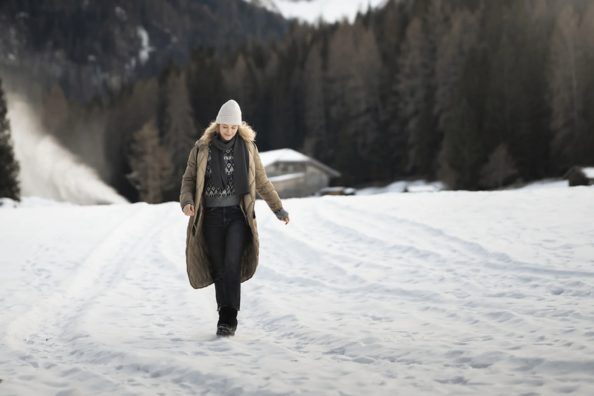 Donna con abbigliamento invernale che cammina su campo innevato con montagne sullo sfondo