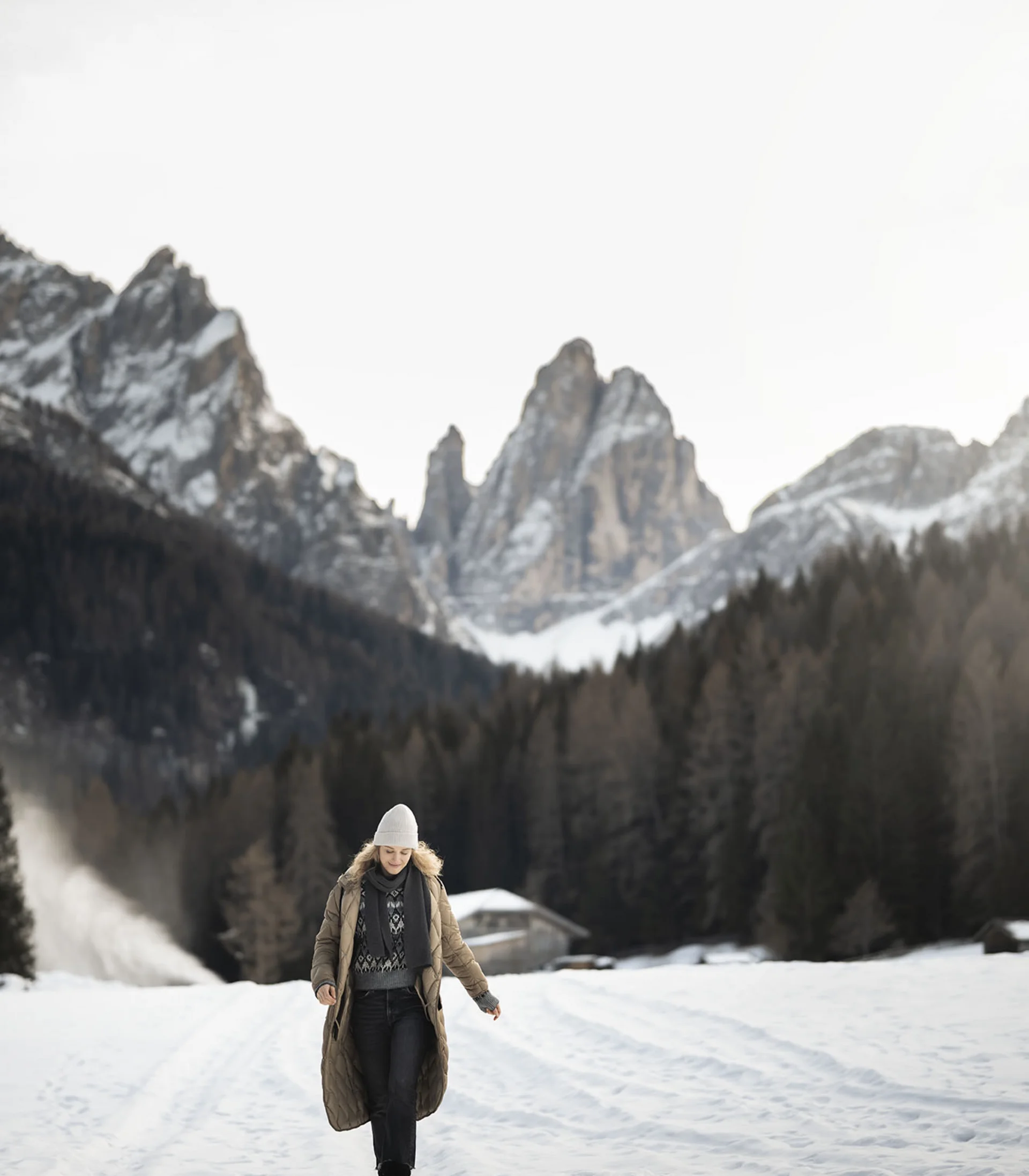 Donna con abbigliamento invernale che cammina su campo innevato con montagne sullo sfondo