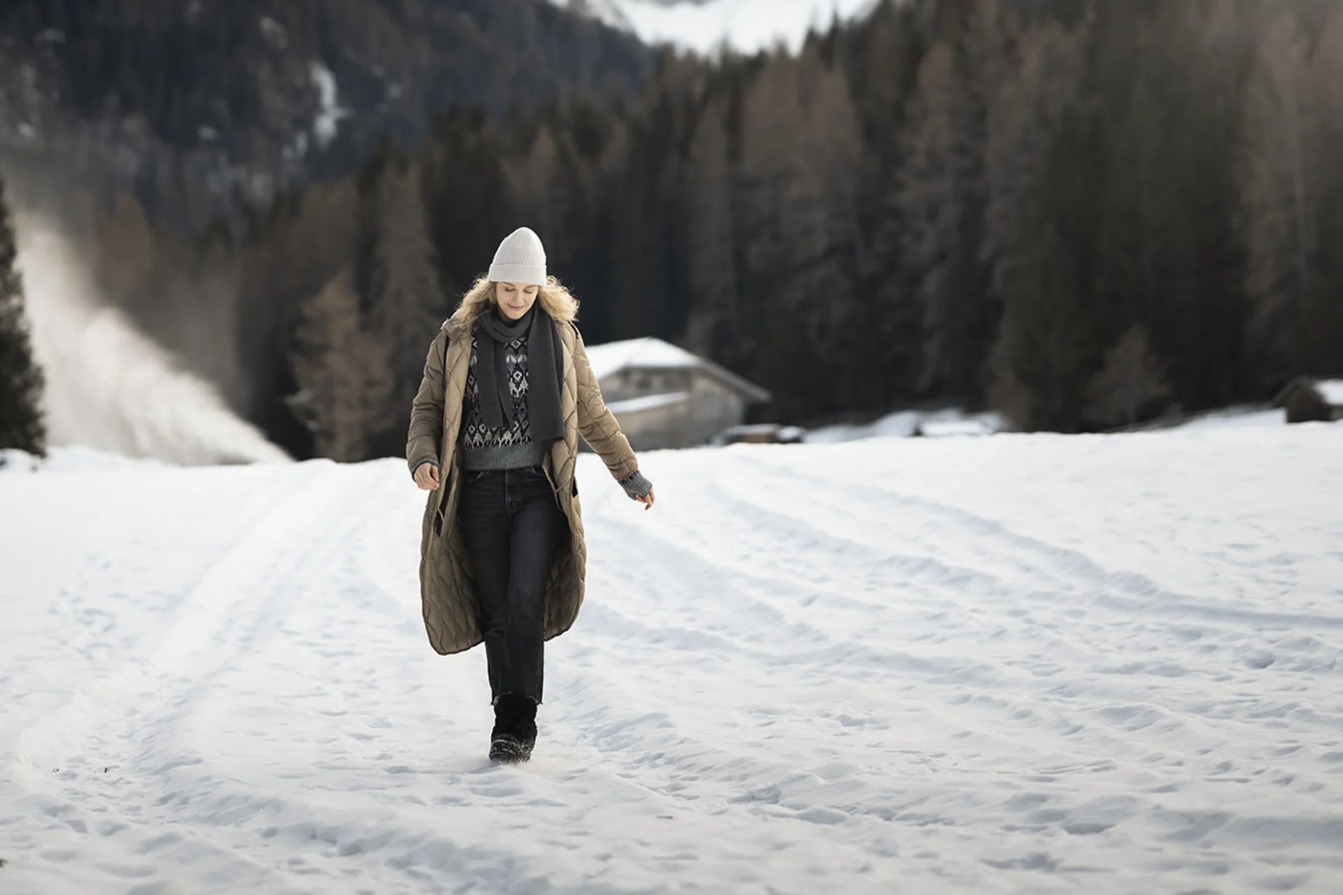 Frau in Winterkleidung geht auf schneebedecktem Feld mit Bergen im Hintergrund