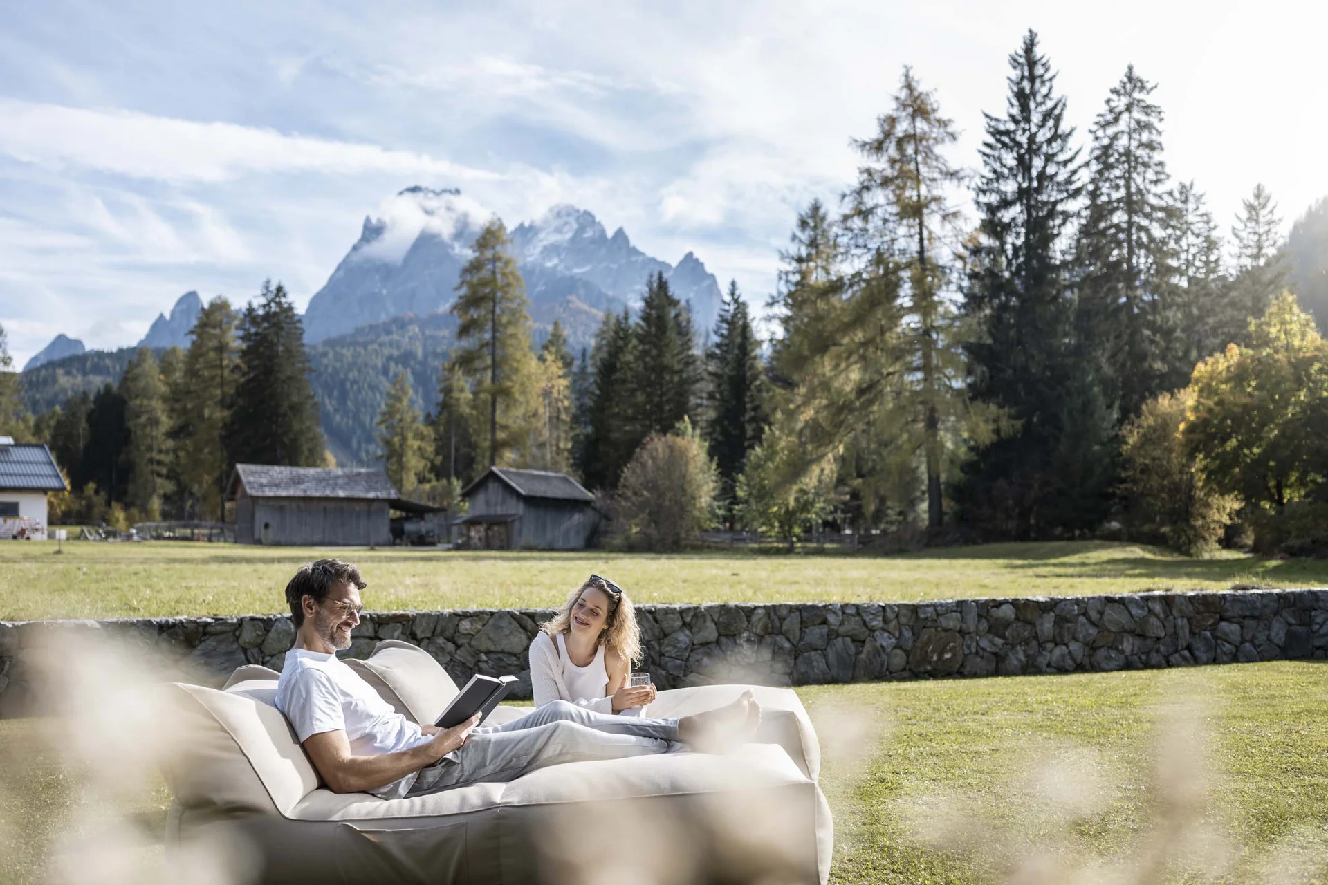 Paar entspannt auf Couch im Garten mit Bergkulisse und Häusern im Hintergrund