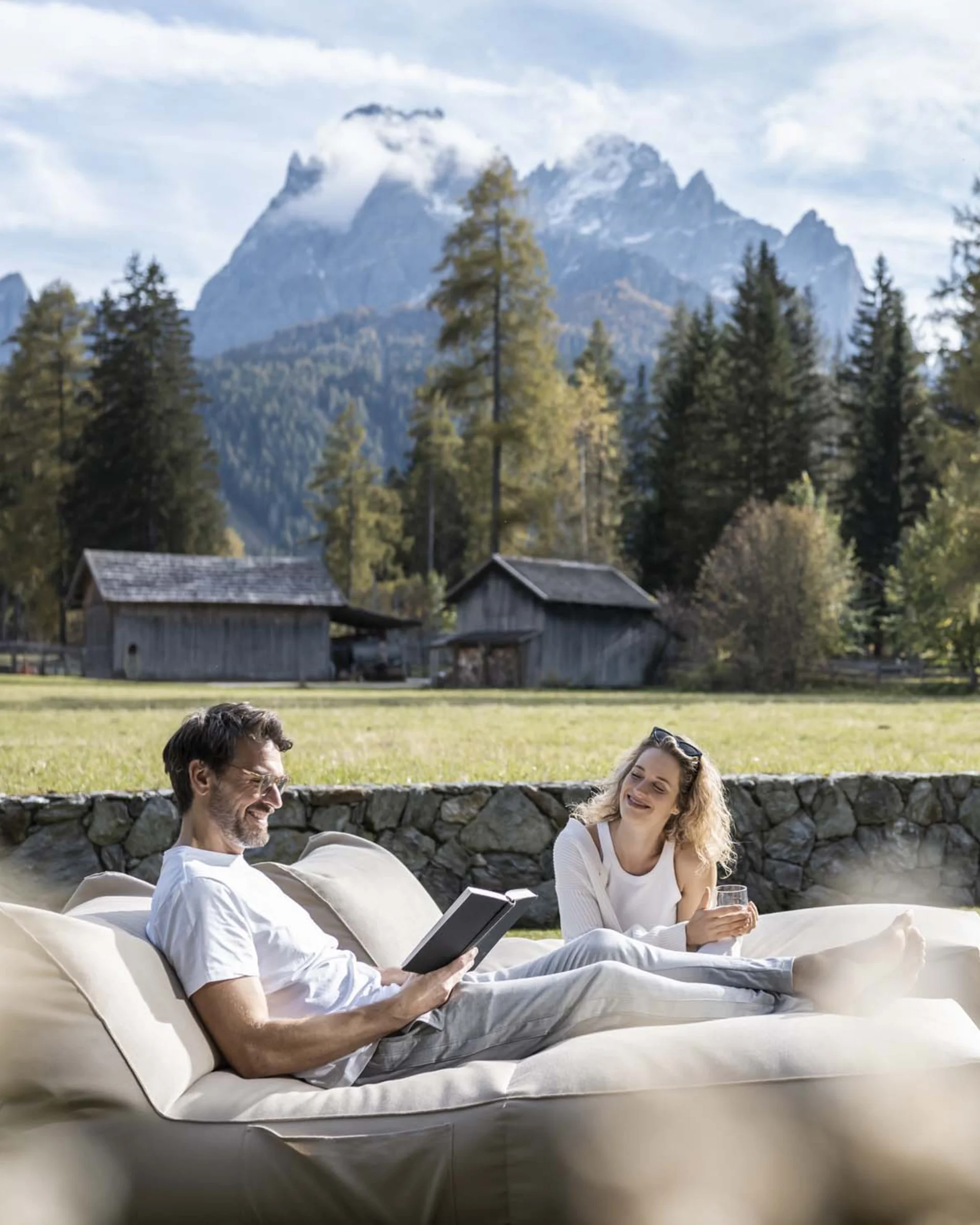 Paar entspannt auf Couch im Garten mit Bergkulisse und Häusern im Hintergrund