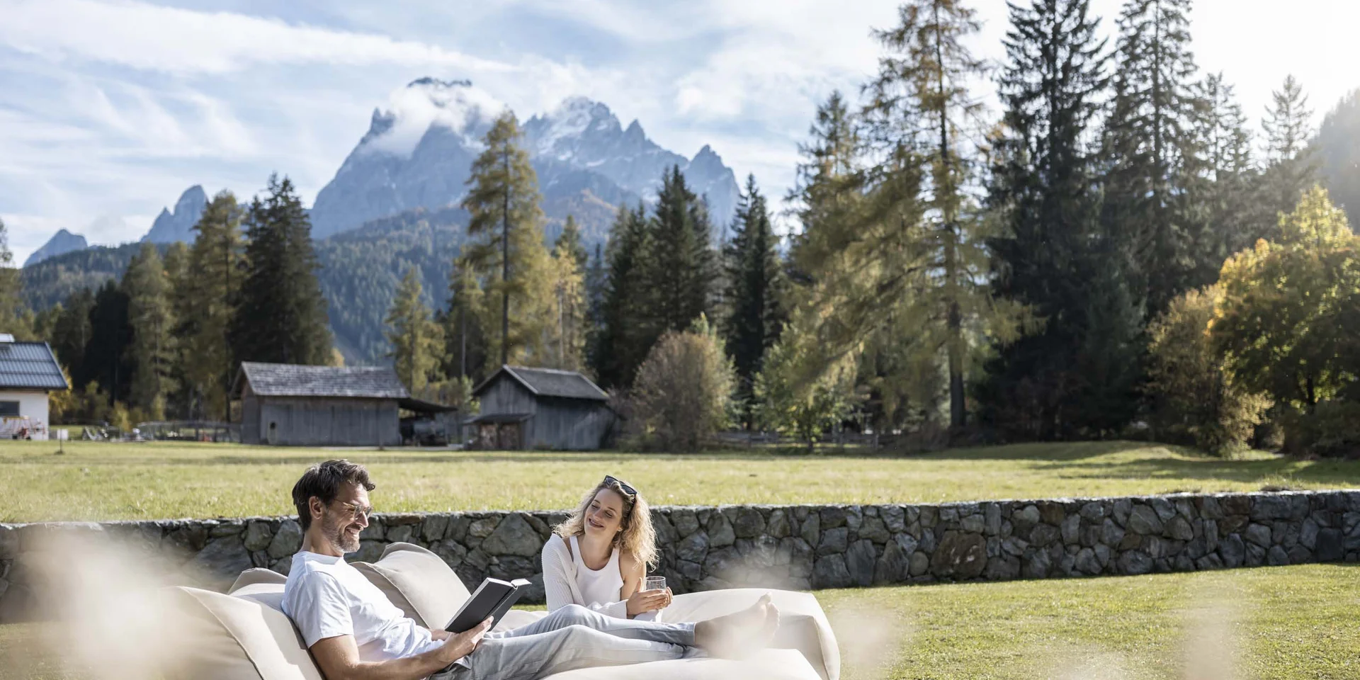 Couple relaxing on sofa in garden with mountains and houses in the background