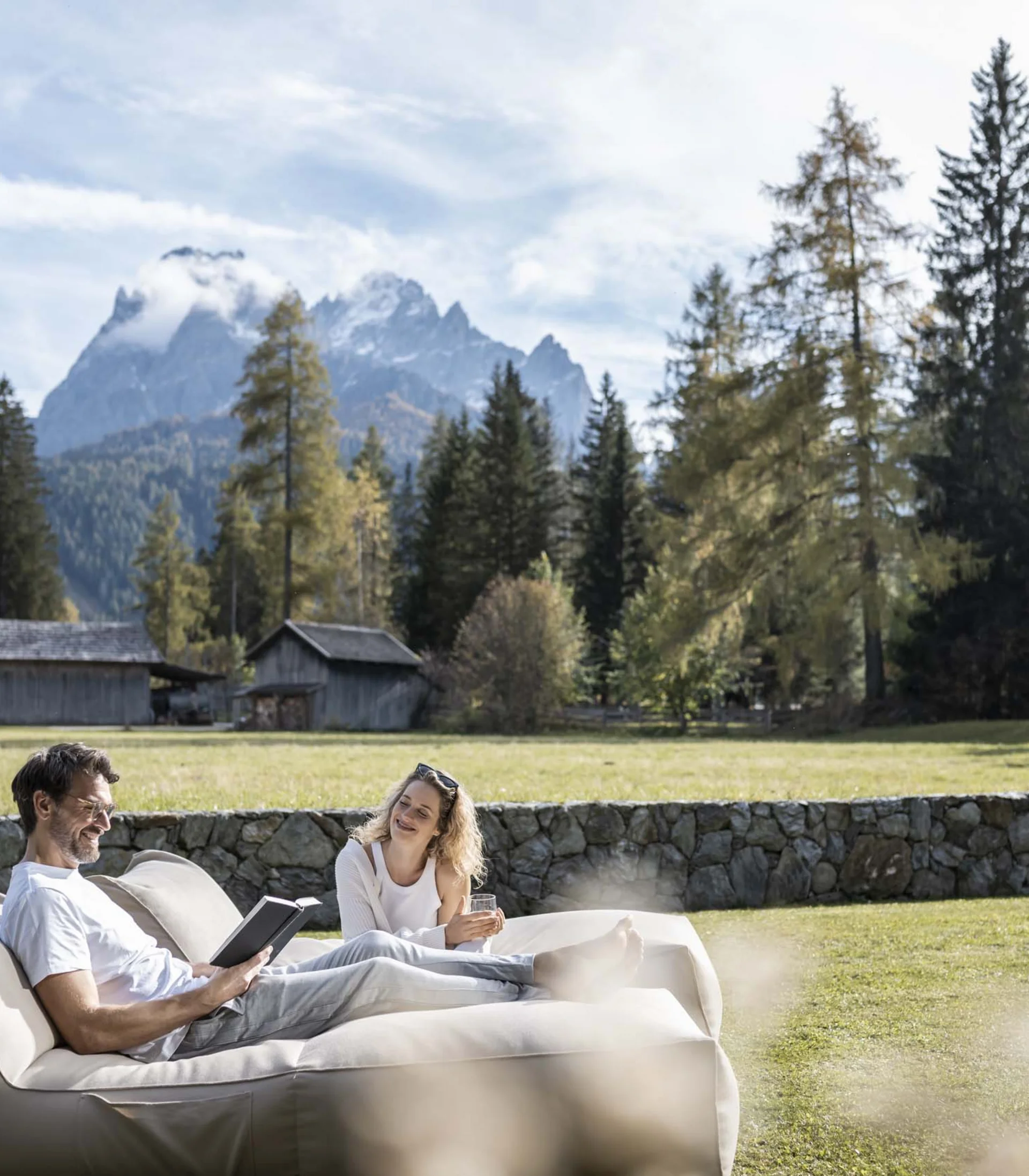 Paar entspannt auf Couch im Garten mit Bergkulisse und Häusern im Hintergrund