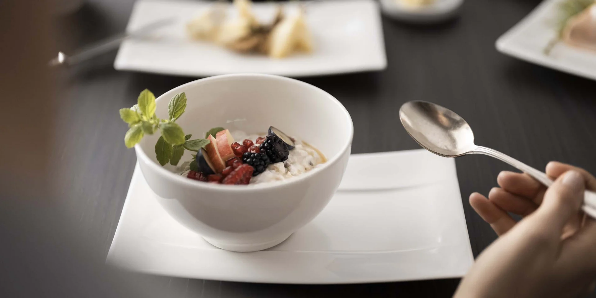 Person hält Löffel vor einer Schale mit Porridge und Beeren