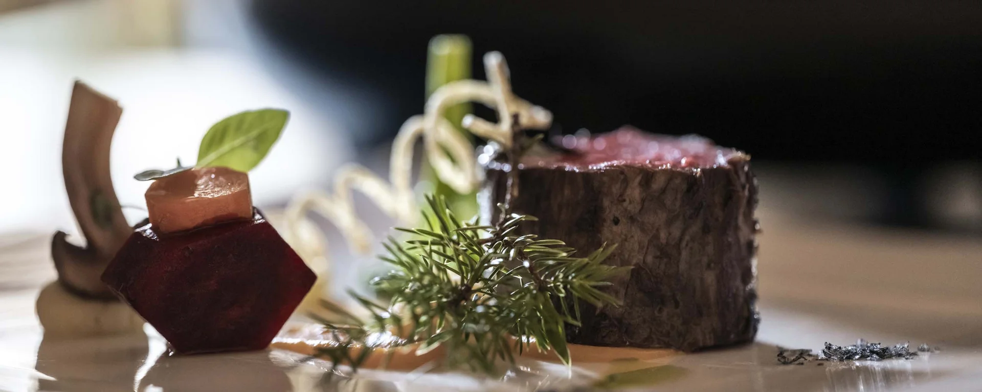 À-la-carte-Restaurant CANA in Sexten Gourmetgericht mit Rindfleisch, Gemüse und Kräutern elegant angerichtet