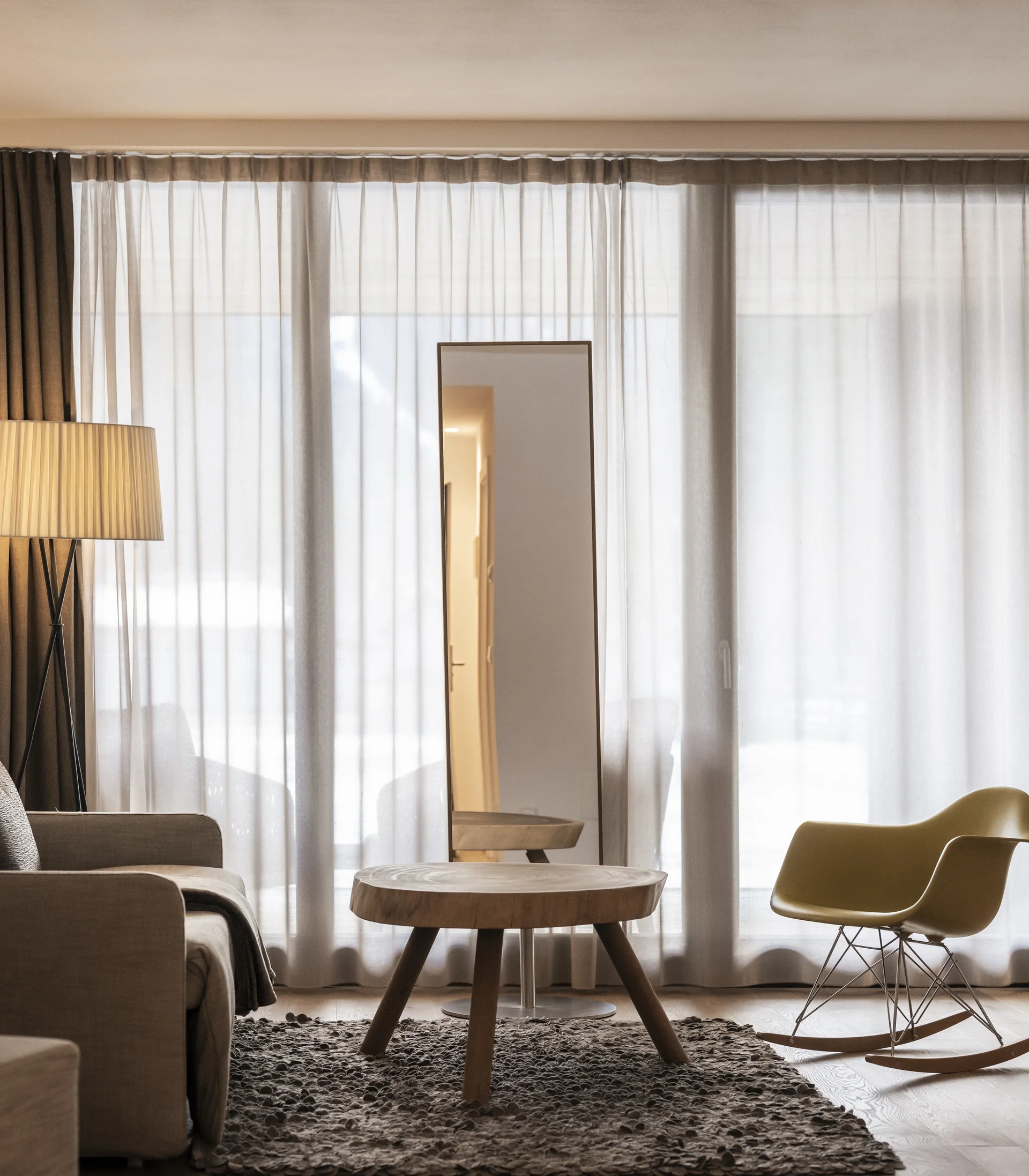 Cozy living room with rocking chair, coffee table, and tall mirror in front of curtains