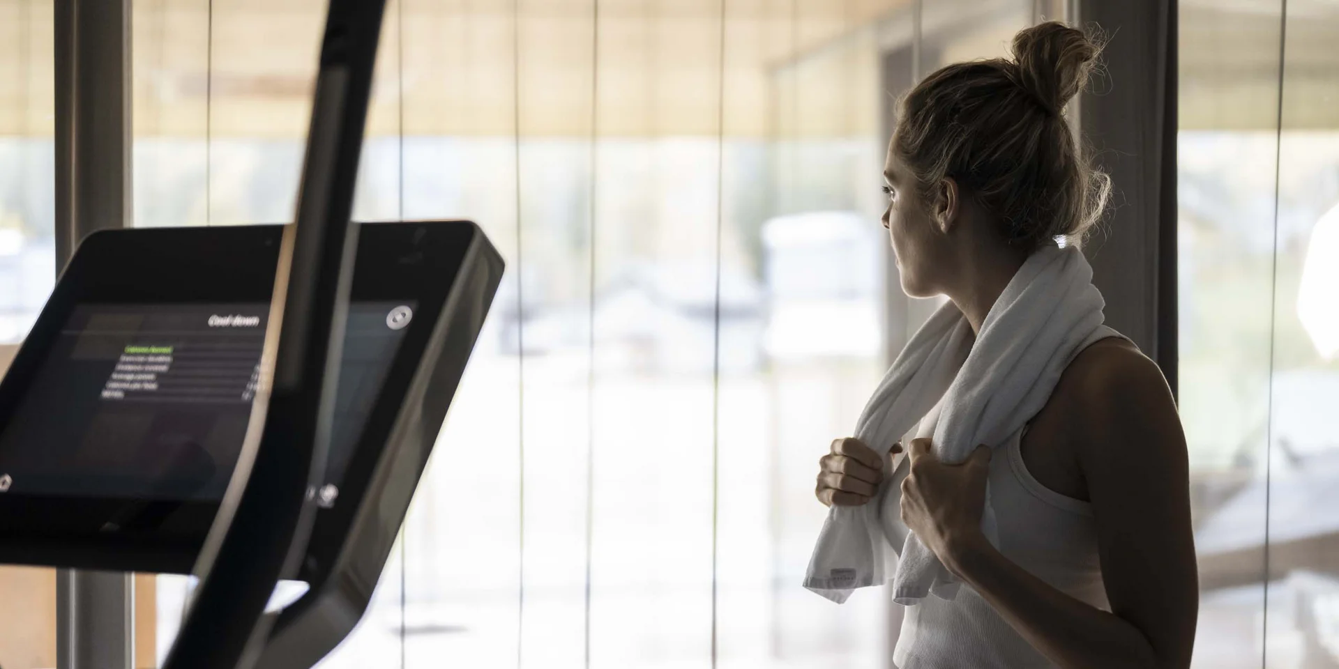 Frau im Fitnessstudio mit Handtuch am Hals blickt aus dem Fenster