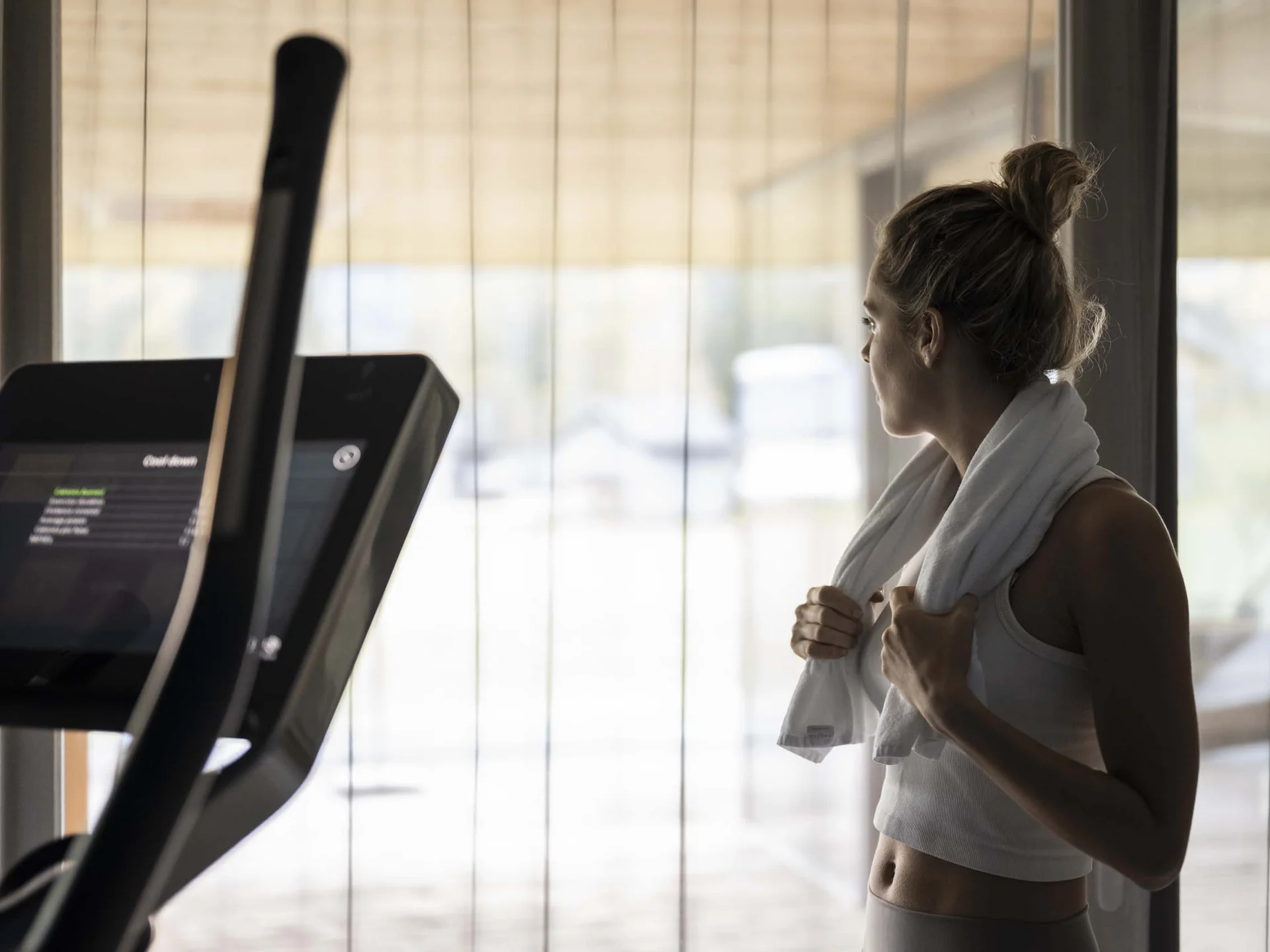 Fitness, Yoga, Outdoor-Erlebnisse: Aktivhotel in Südtirol Frau im Fitnessstudio mit Handtuch am Hals blickt aus dem Fenster