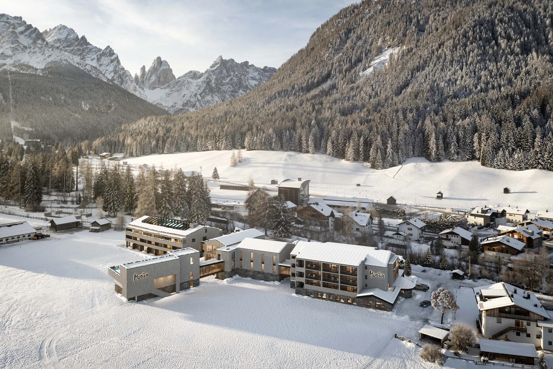 Hotel Monika im verschneiten Tal mit Bergen und Wald im Hintergrund