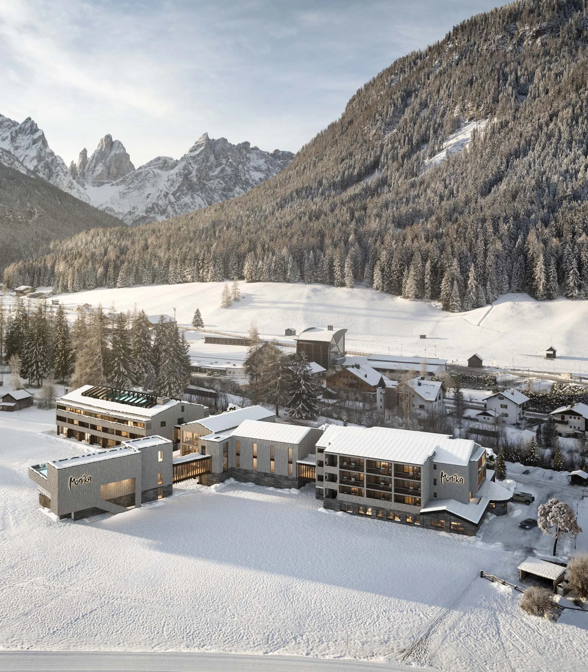 Hotel Monika im verschneiten Tal mit Bergen und Wald im Hintergrund