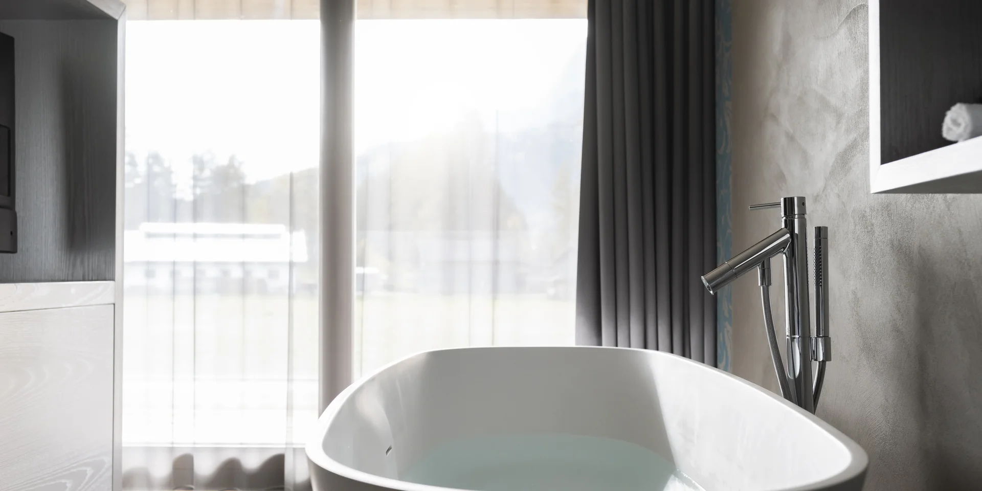 Modern freestanding bathtub in front of large windows with curtains