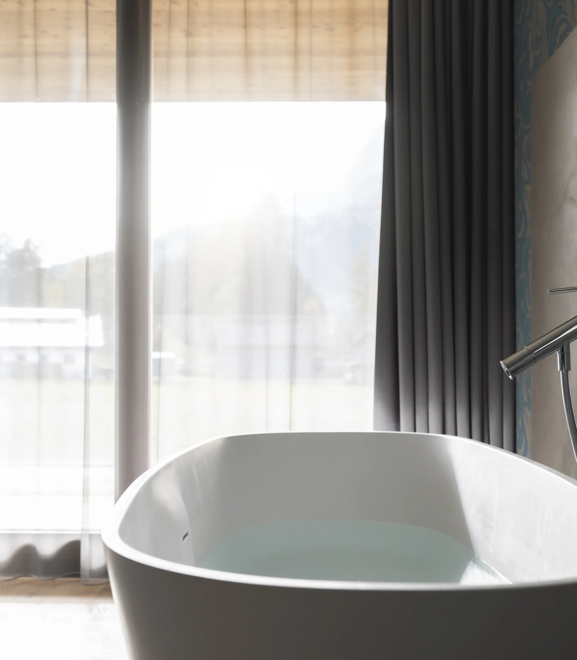 Moderne freistehende Badewanne vor großen Fenstern mit Vorhängen