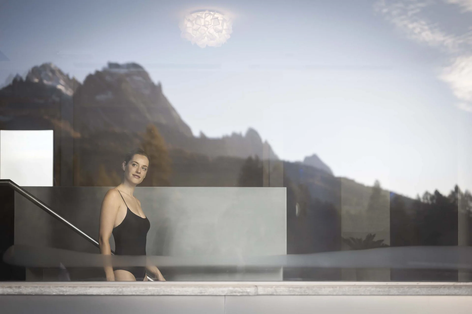 Frau im schwarzen Badeanzug in einem modernen Pool mit Bergblick