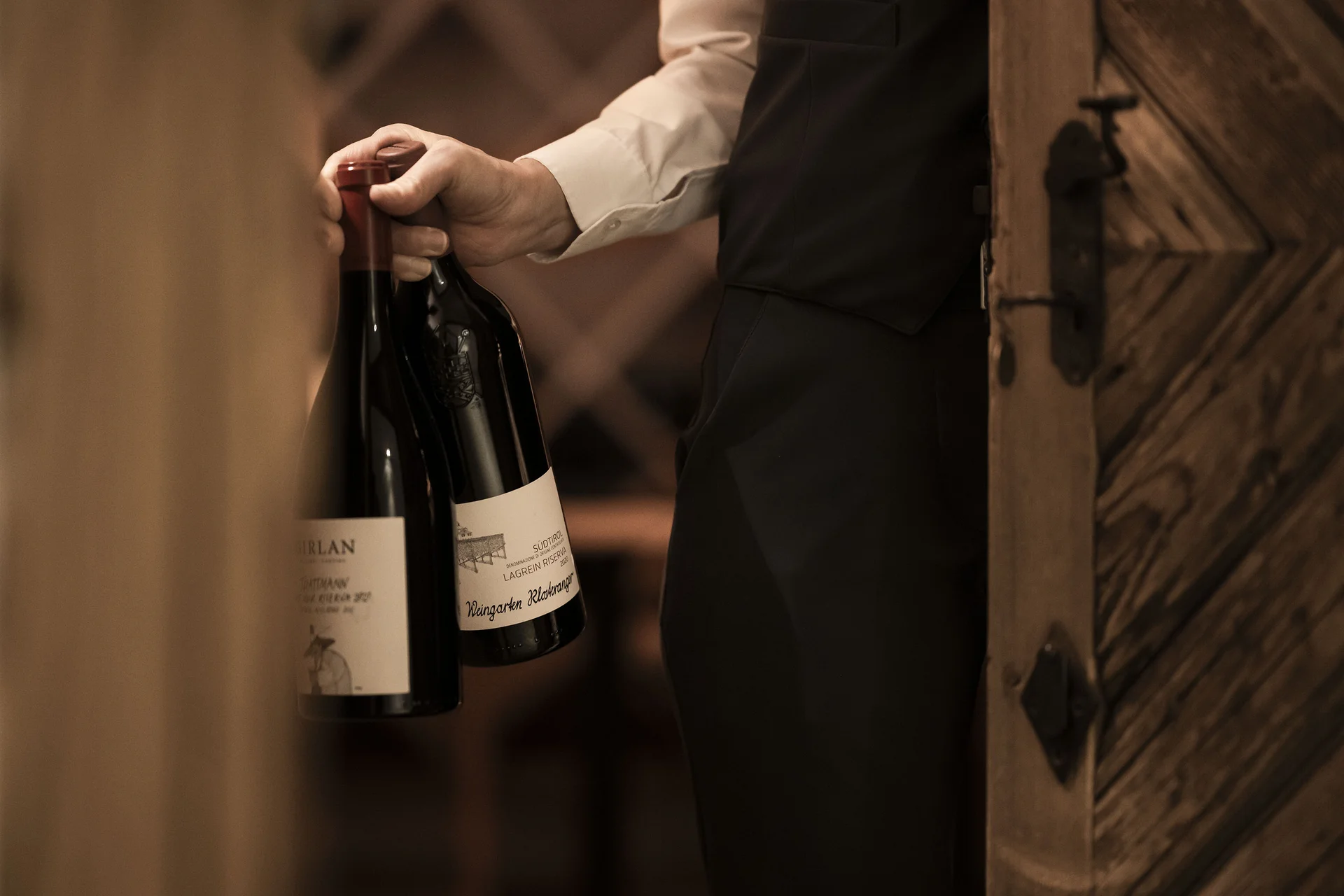 Mann trägt zwei Flaschen Wein in einem Weinkeller