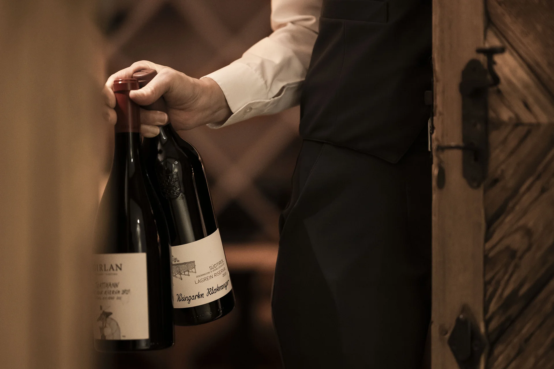 Uomo che porta due bottiglie di vino in una cantina