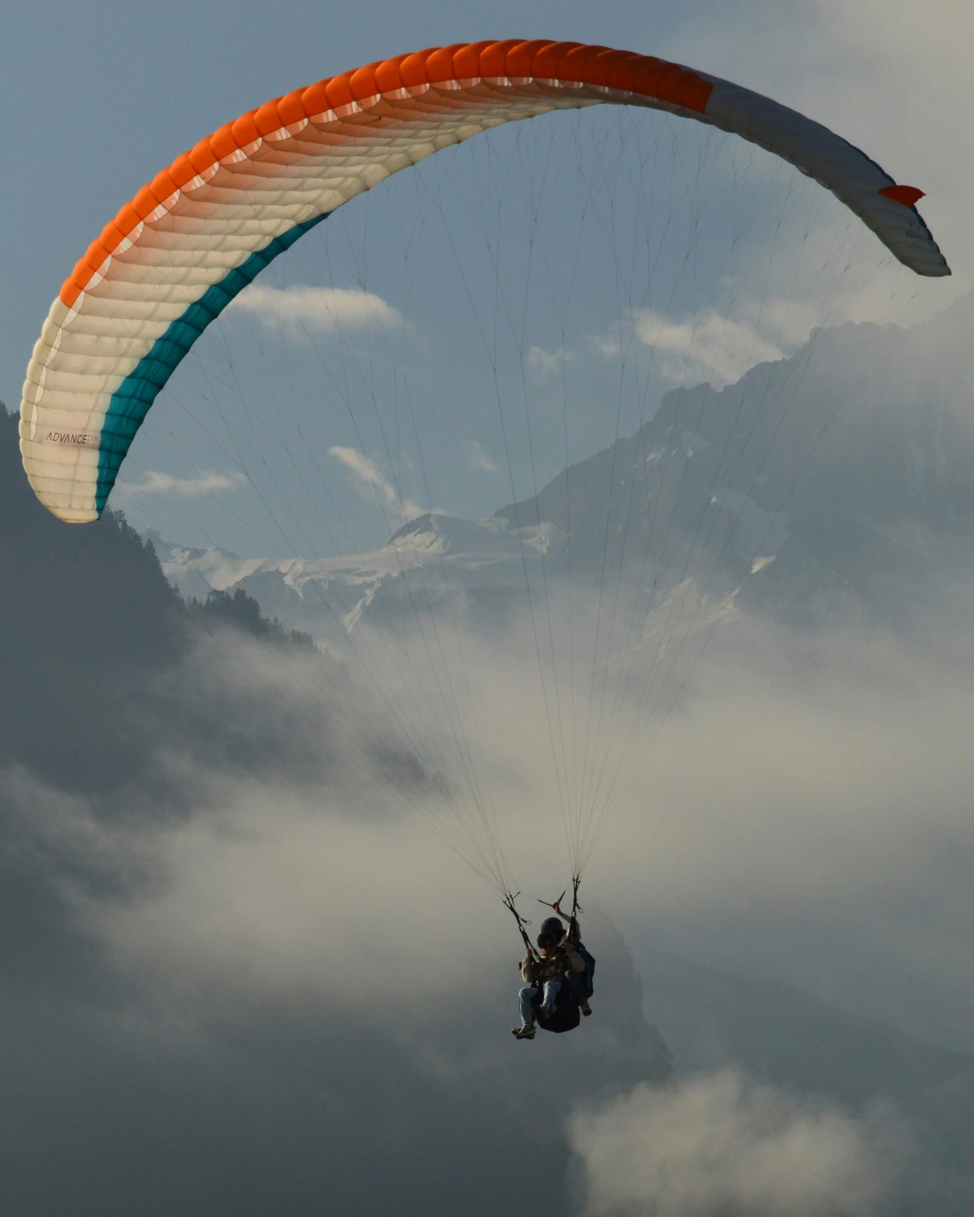 Zwei Personen beim Gleitschirmfliegen über nebligen Bergen