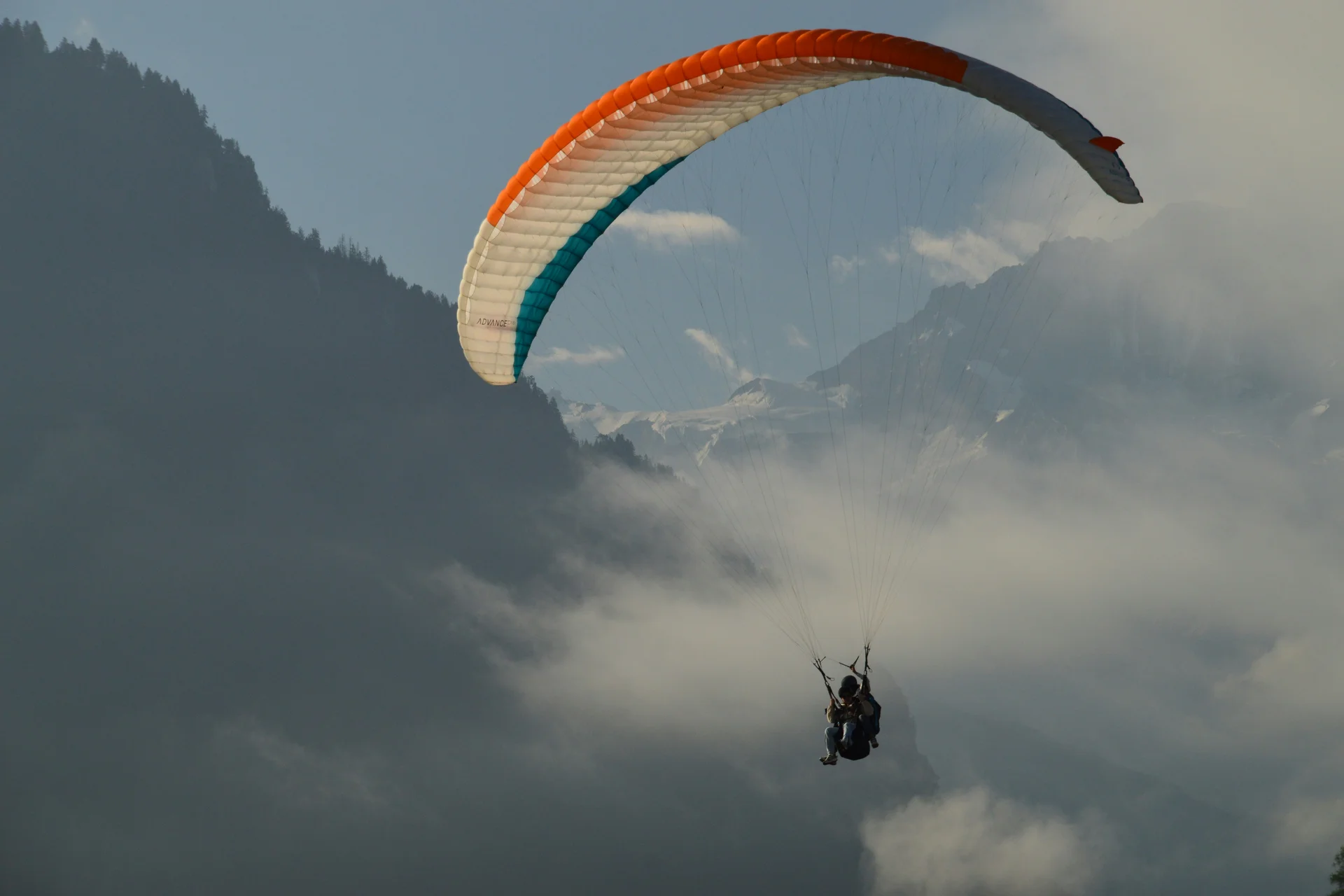 Zwei Personen beim Gleitschirmfliegen über nebligen Bergen