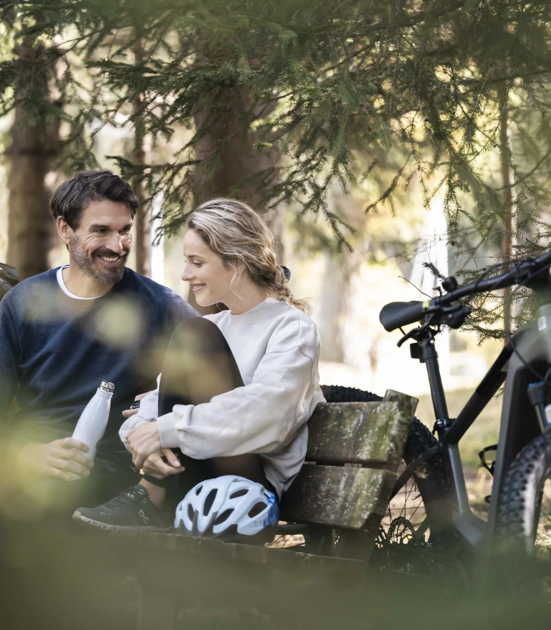 Paar macht Pause auf einer Bank im Wald mit Fahrrädern im Hintergrund